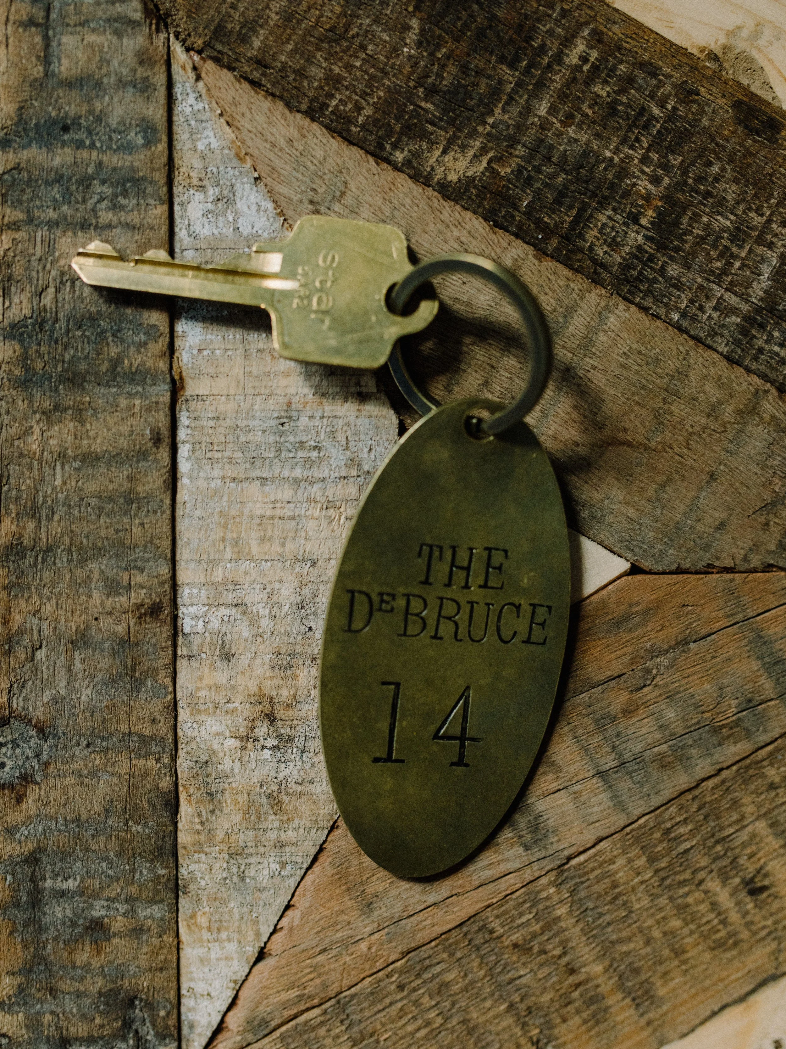 A key with a metal tag engraved with 'THE D BRUCE 14' attached to a wooden wall with various weathered wood planks.