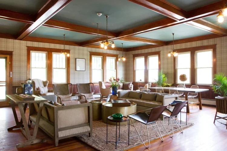 Living room with multiple sofas and chairs, wood-paneled walls, large windows, and furniture arranged around a central rug.