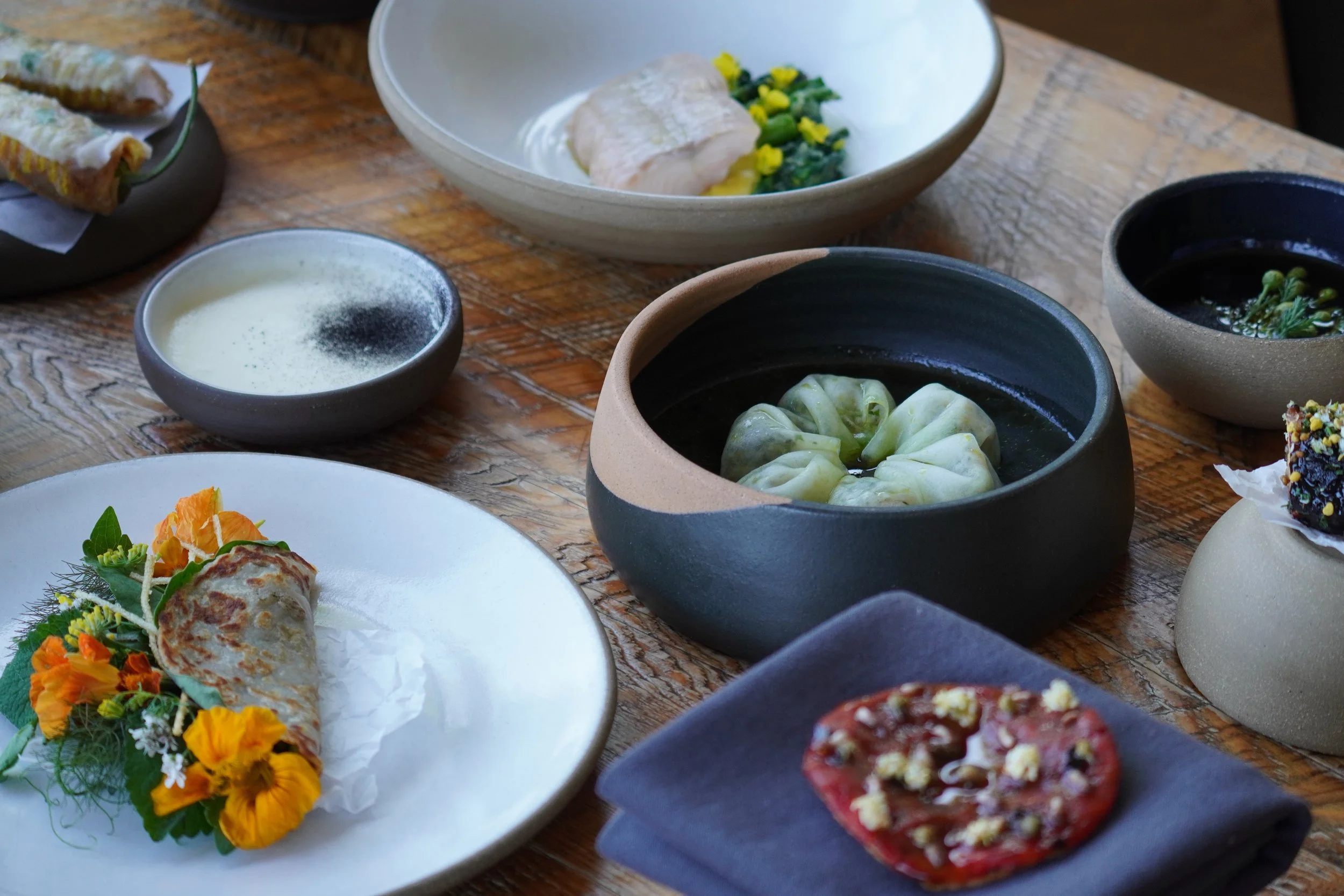 A gourmet dish featuring a piece of salmon garnished with edible flowers, served on a bed of green foam on a large white plate.