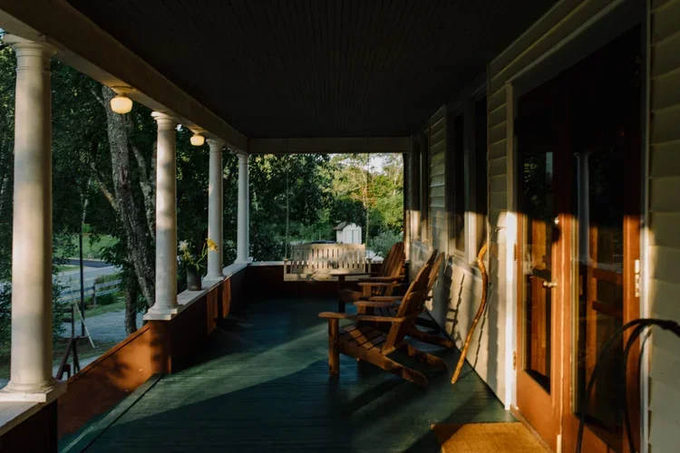 A cozy porch with wooden rocking chairs, decorative lights, and a view of greenery and trees outside.