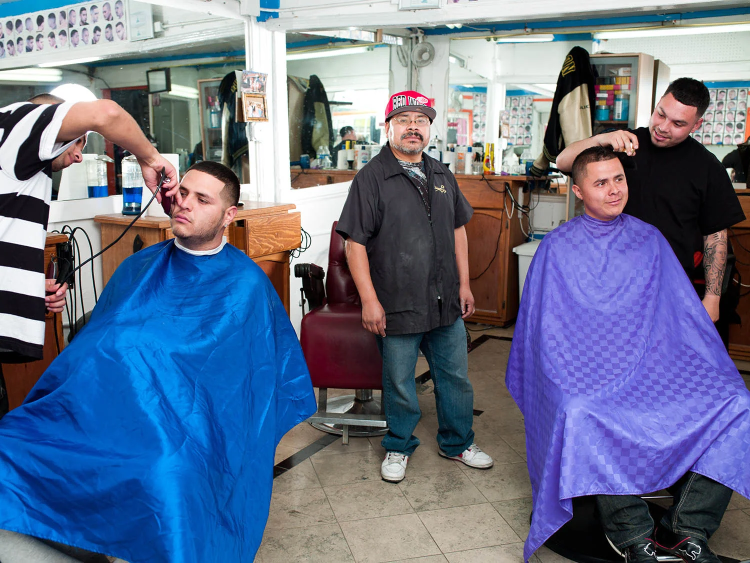 On March 1, 2012, Ignacio Gonzalez watches over his barber shop on Central Ave. and 42nd St while Johnny Vera trims Juan Guitron (L) and Alex Vargas finishes work on Oscar Sanchez.
