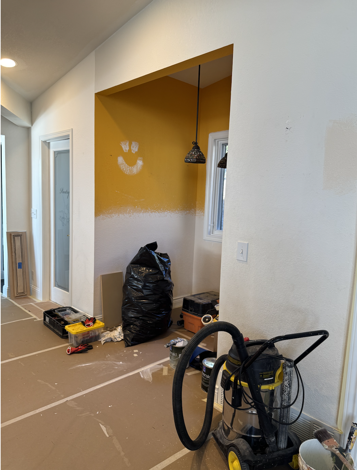Room under renovation with partially painted yellow and white wall, tools, and equipment on the floor.
