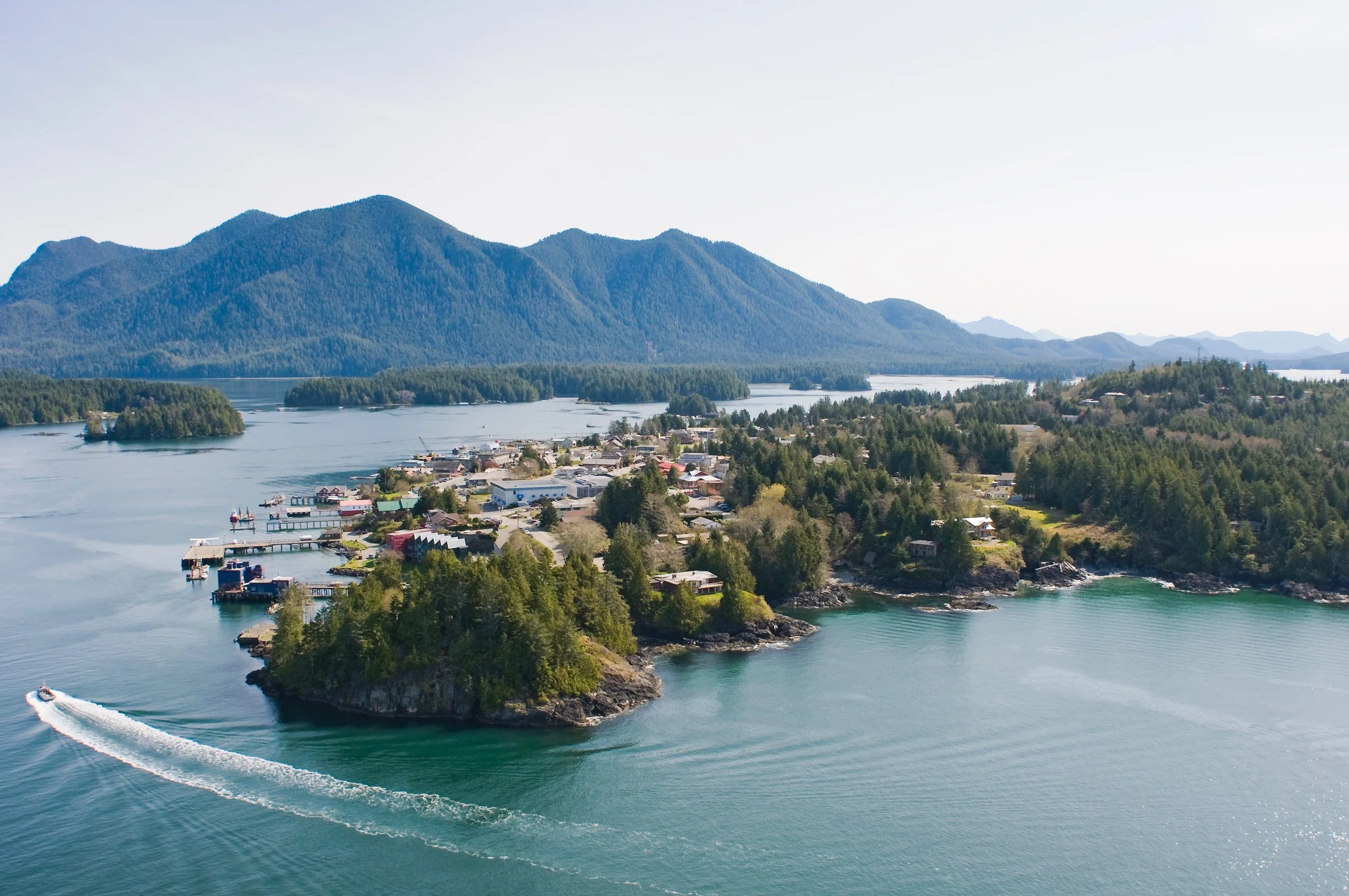 Scenic aerial view of a coastal town surrounded by water, islands, and lush green forests with mountains in the background.