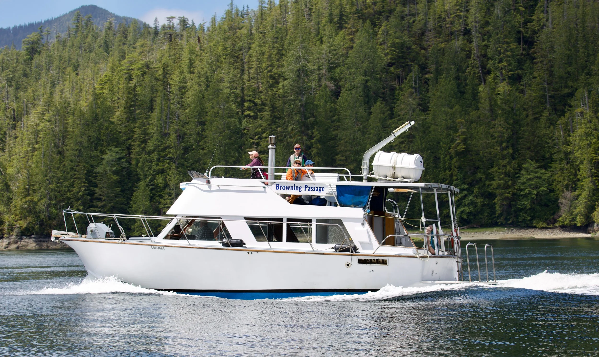 A white motorboat named 'Browning Passage' sailing on a body of water with a background of dense green forested mountains.