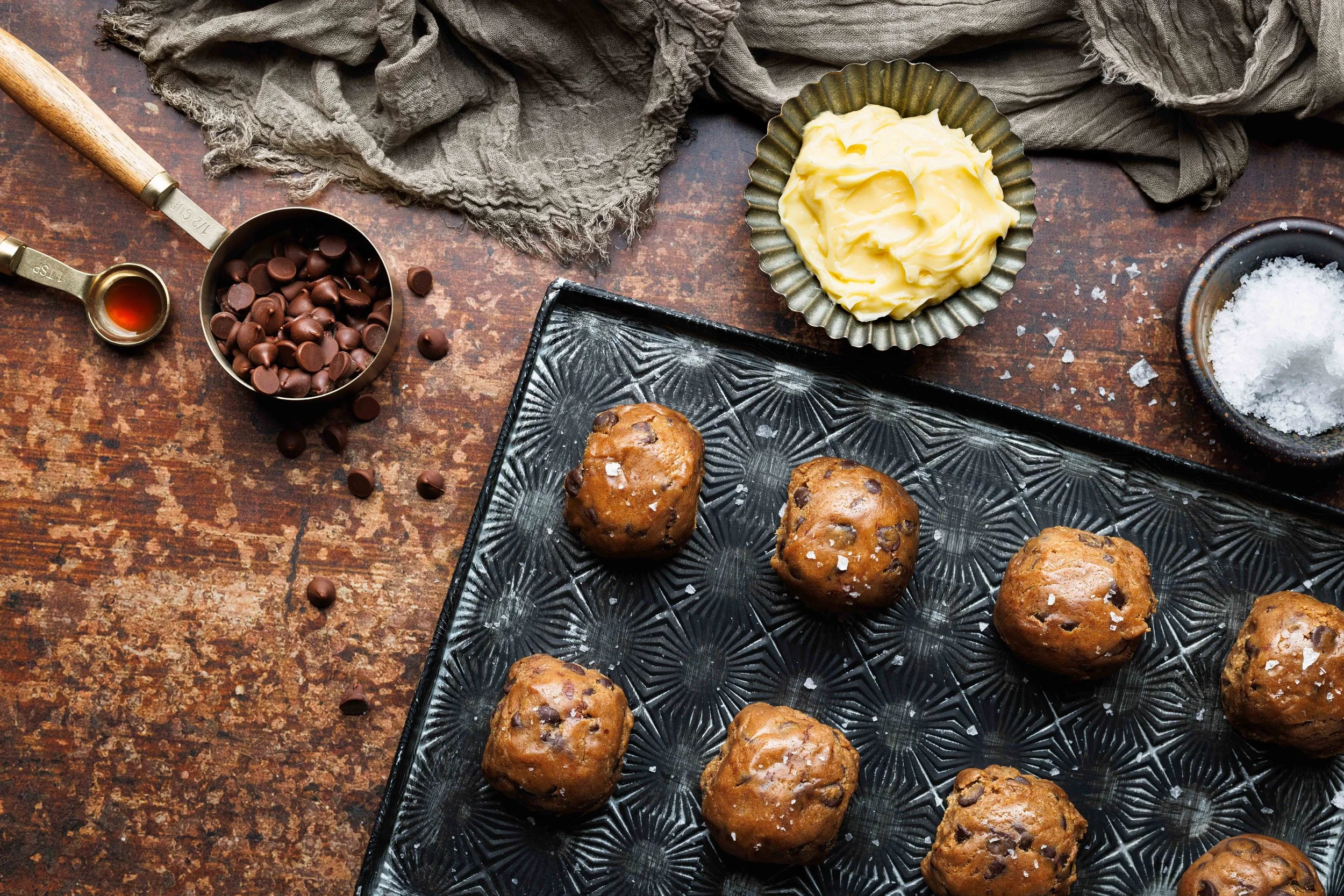  Advertising photo of chocolate chip cookie dough with ingredients in a rustic, moody frame. Shot by commercial food photographer Amy Carson, based in San Diego, California. 