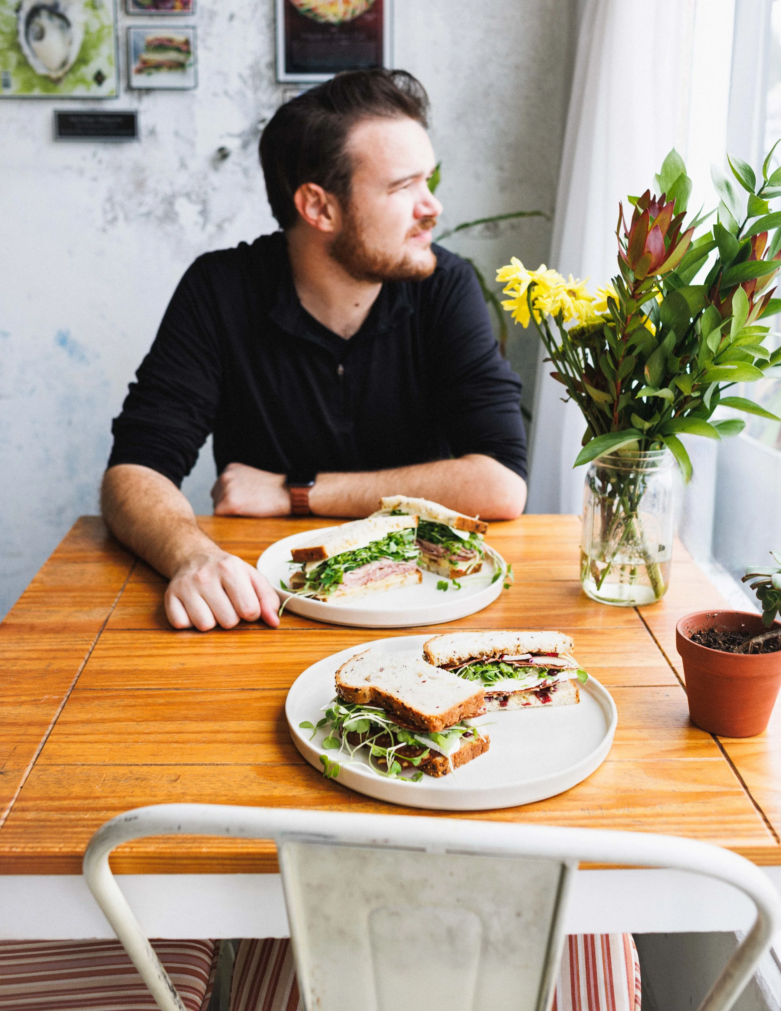 Editorial lifestyle photo of a young man sitting at a cafe table with sandwiches. Photo by San Diego food and lifestyle photographer Amy Carson. 