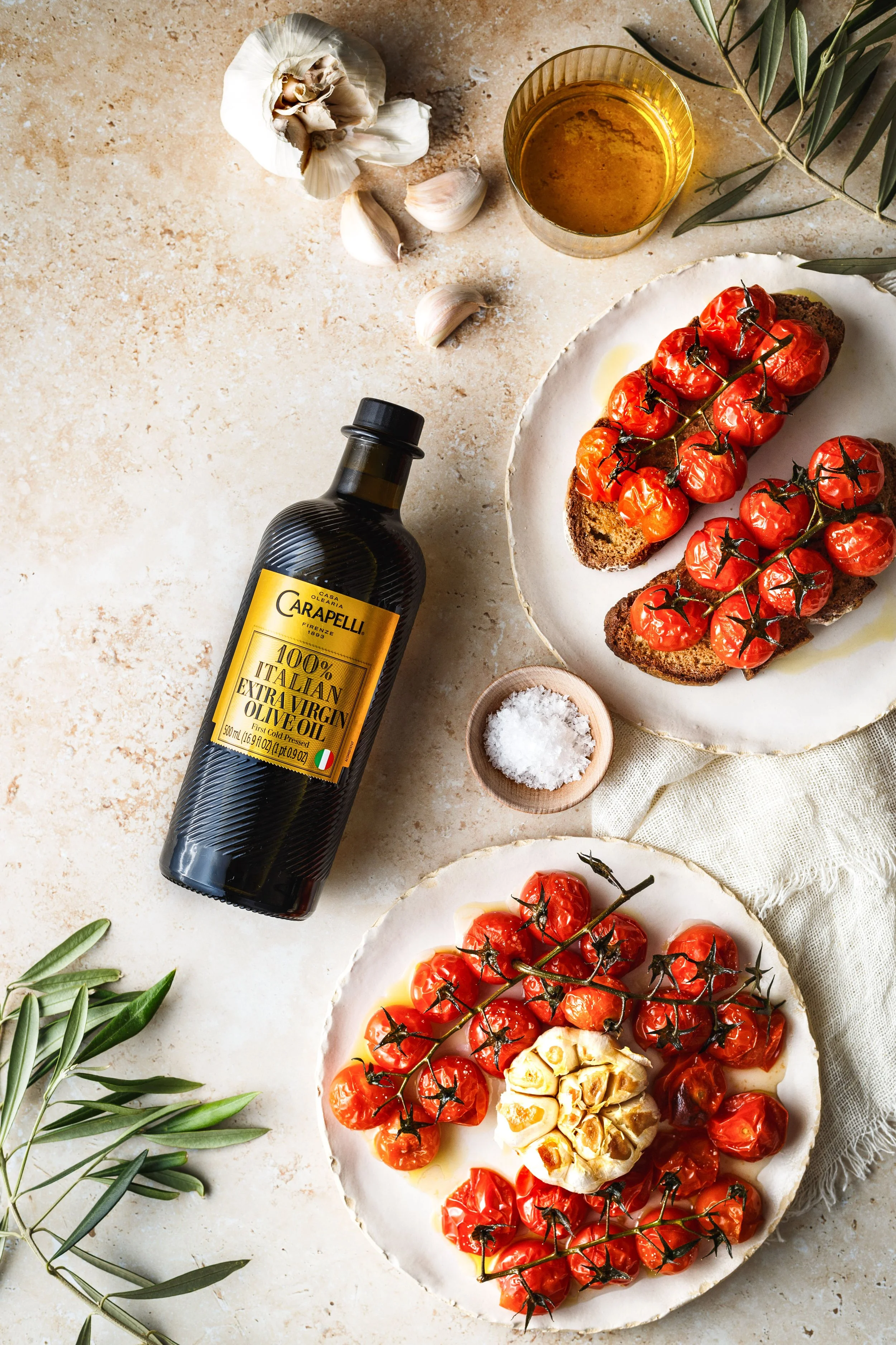  Image by Amy Carson, San Diego food photographer. Commercial advertising food photo of olive oil bottle with roasted tomatoes, garlic and bread in a beautifully styled scene. 