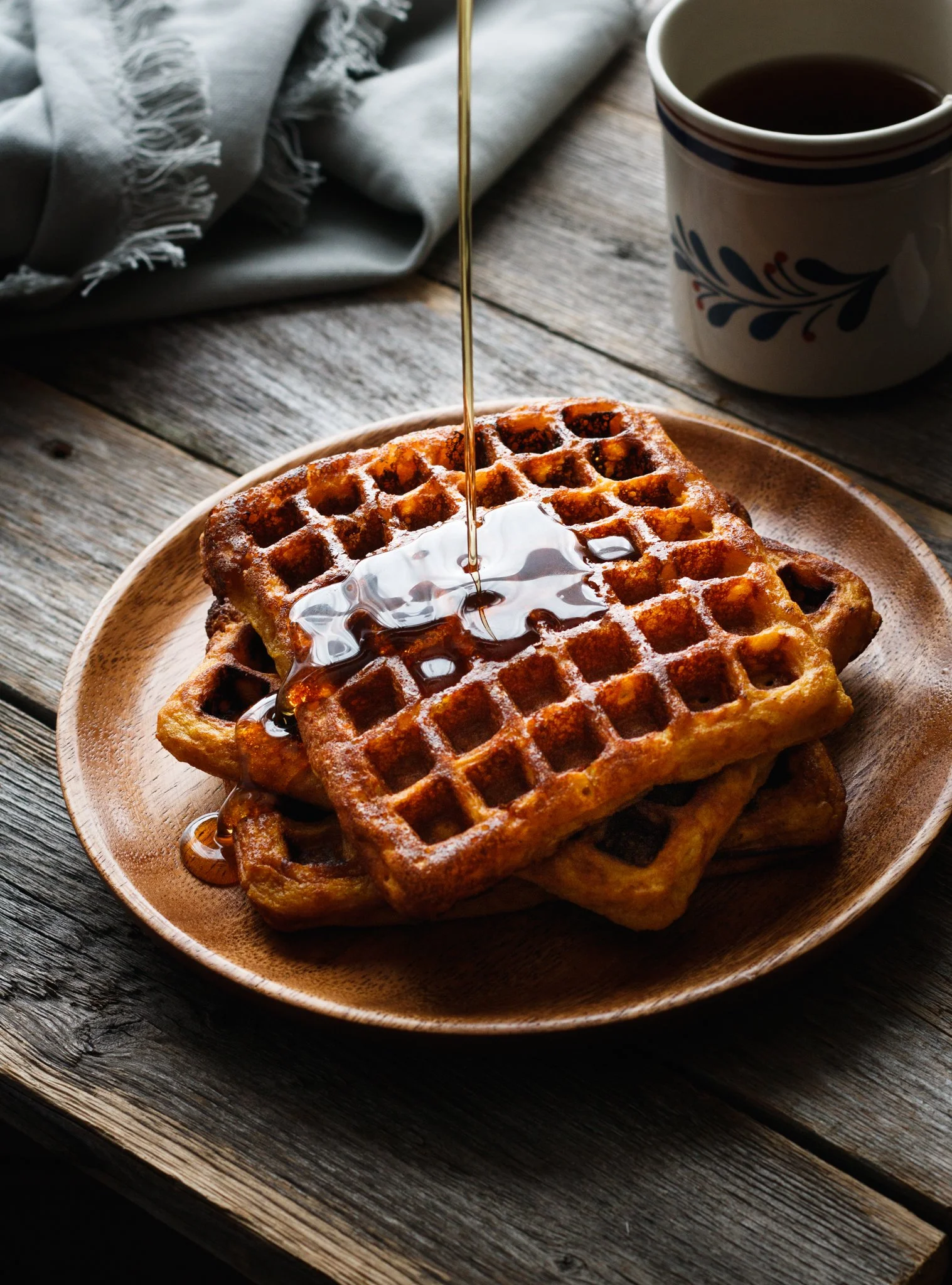  Image by Amy Carson, San Diego food photographer. Commercial food photo of sweet potato waffles with maple syrup pour on a rustic wood table. Moody lighting.  