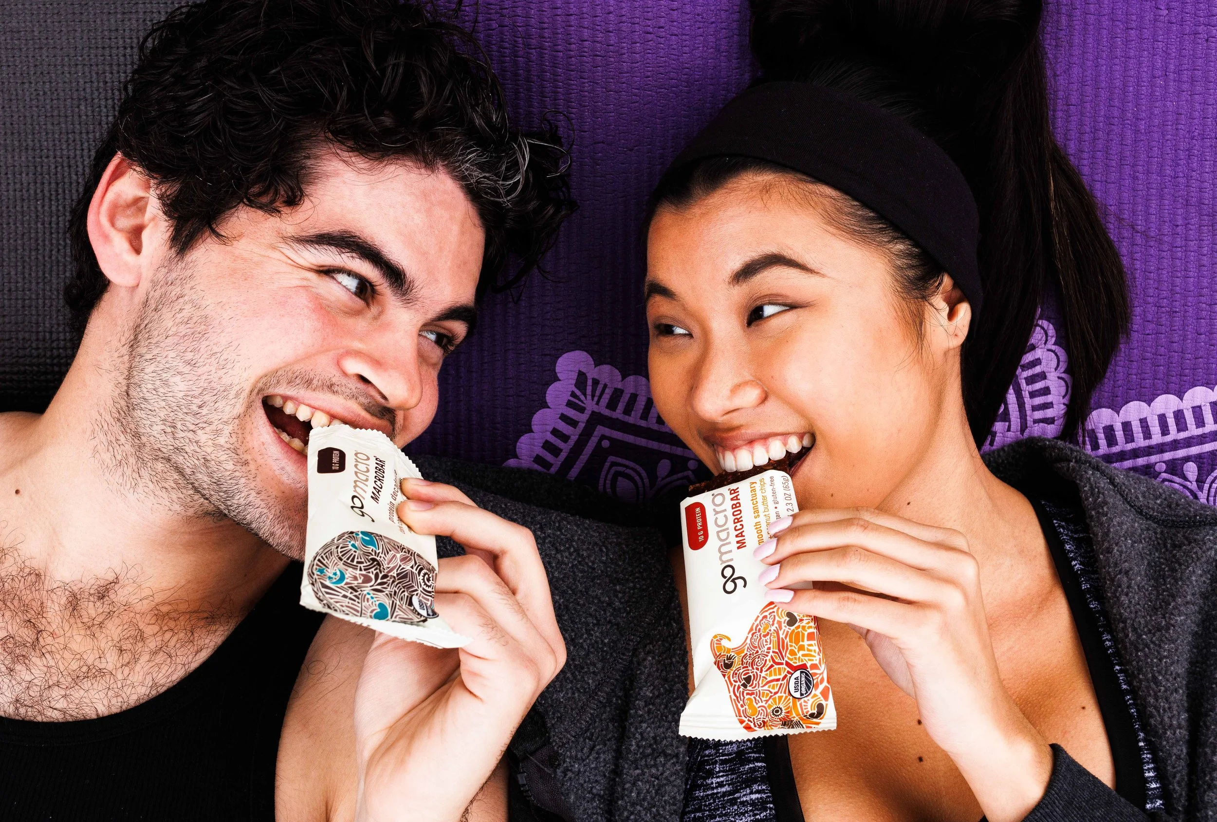  Commercial advertising photo of a young couple on a yoga mat wearing athletic clothing. Eating a GoMacro vegan protein bar. Photo by San Diego food photographer Amy Carson. 