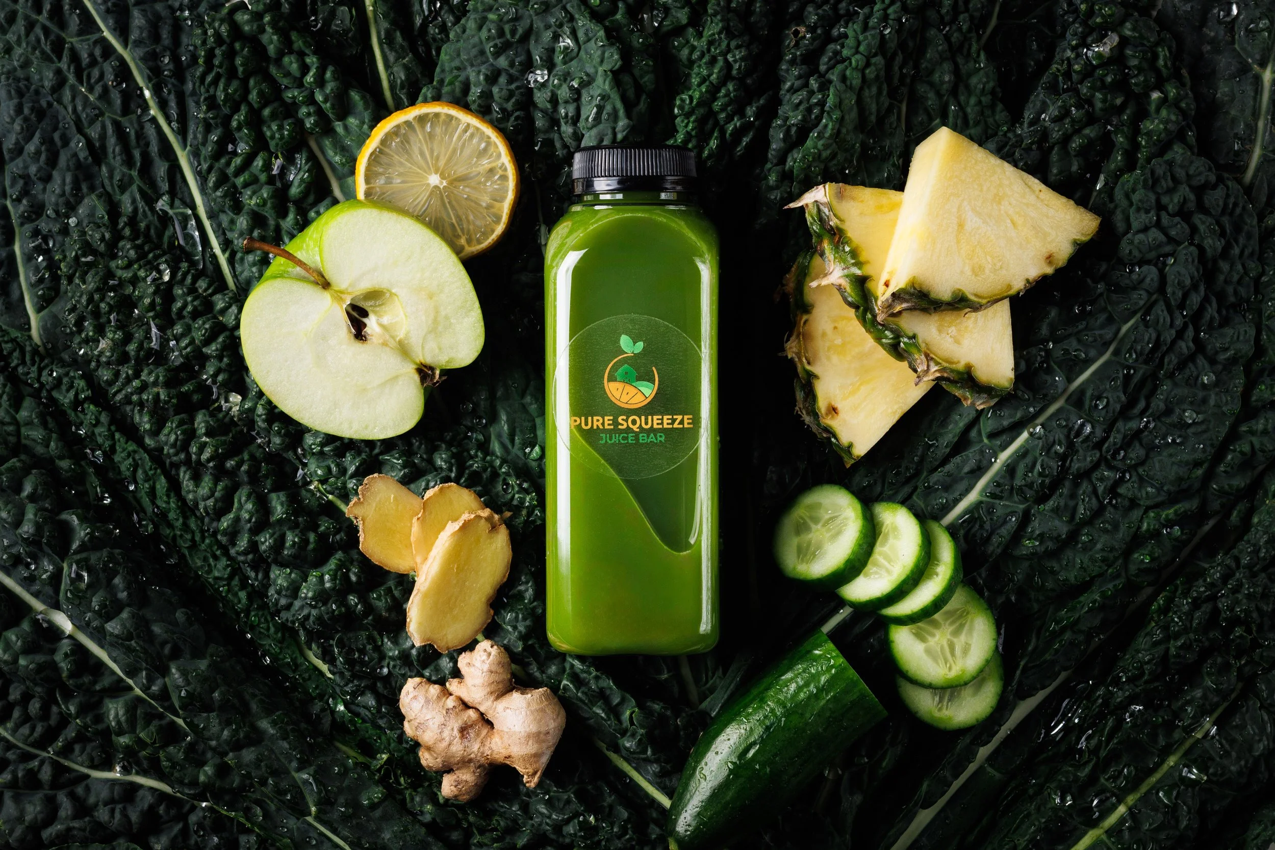 Commercial lifestyle product photo of a bottled green juice surrounded by fresh fruit and veg on a dark, moody kale background. Shot by Amy Carson, San Diego food, drink, and lifestyle product photographer.