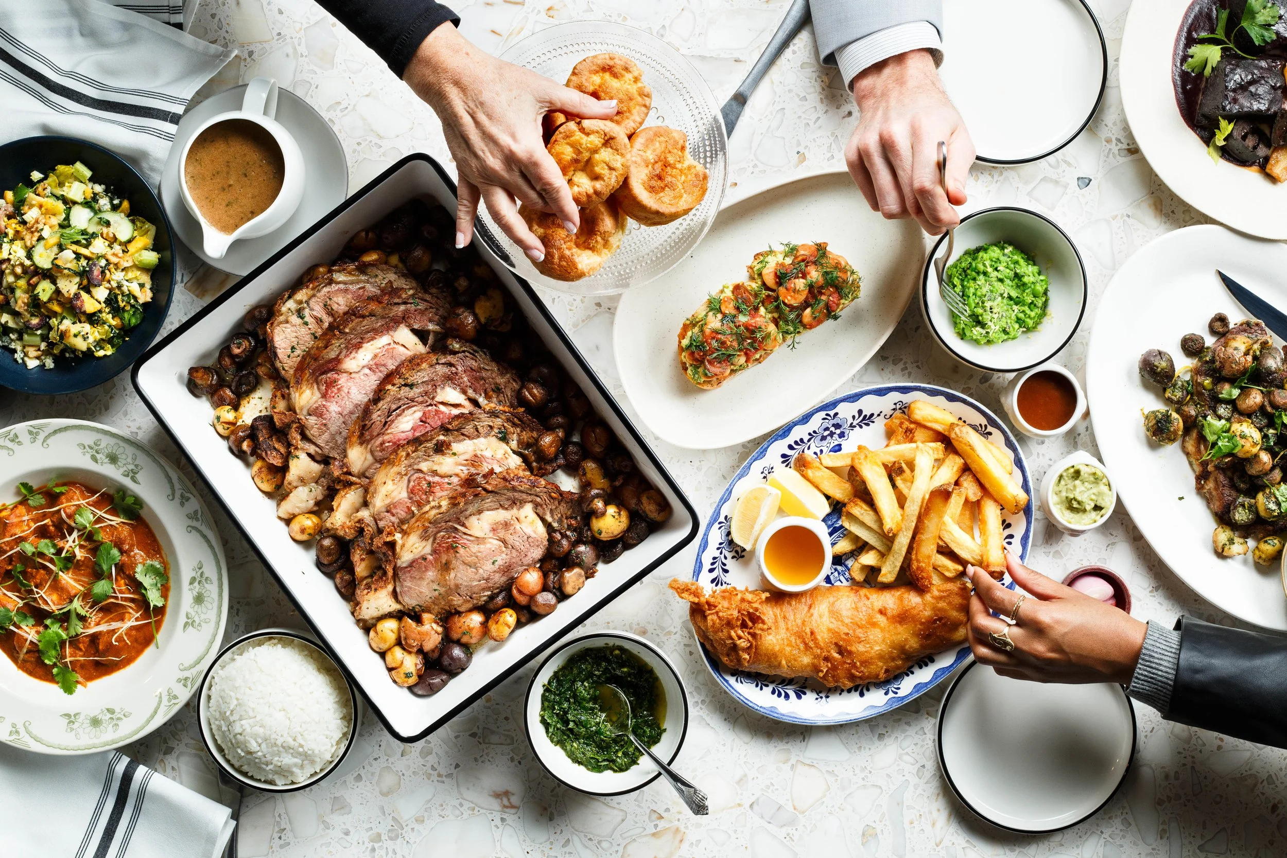 Commercial food lifestyle photo of hands reaching for food on table in restaurant. By Amy Carson.