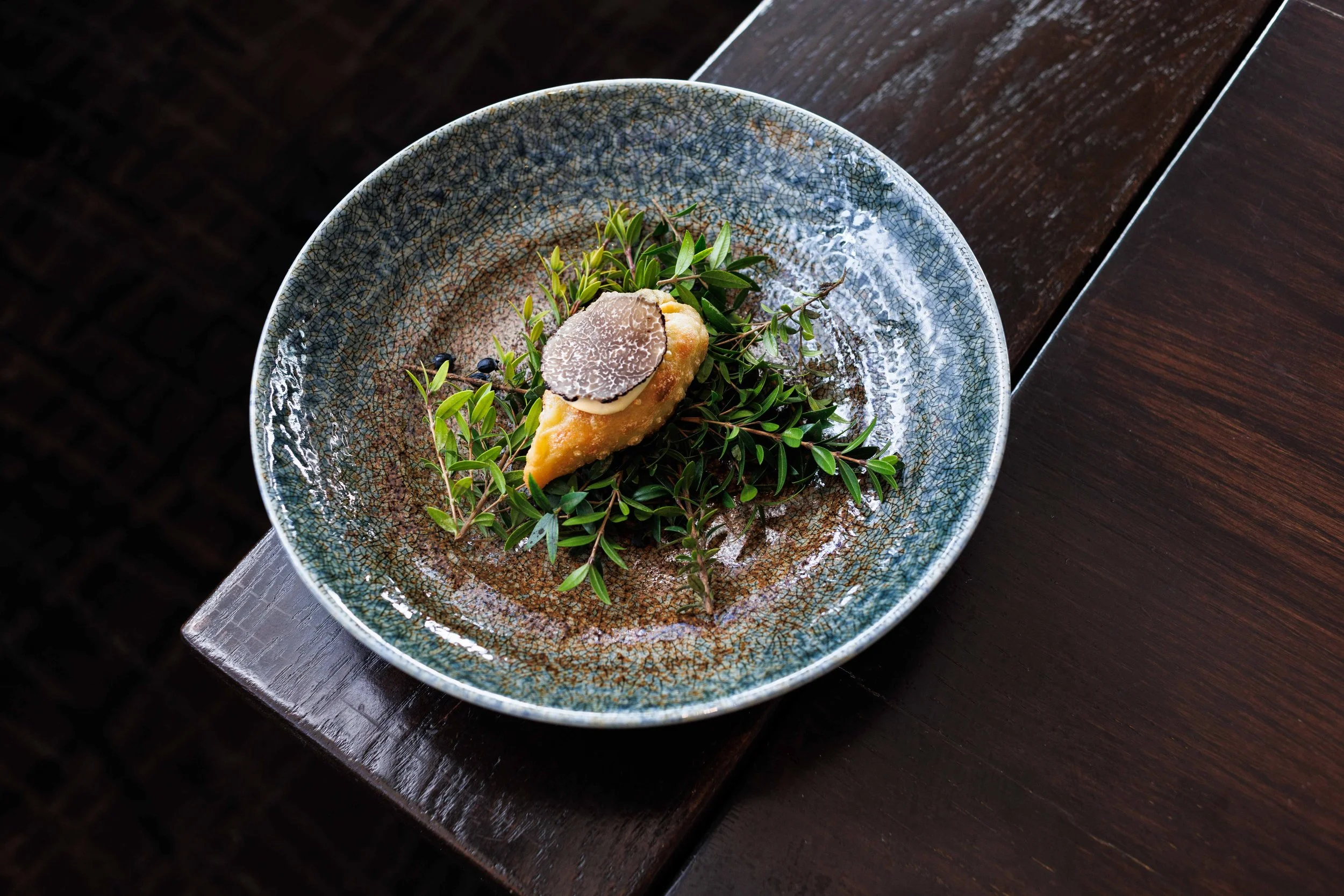 Elegantly plated appetizer on glazed ceramic bowl and dark wood. Fine dining restaurant photography in San Diego.