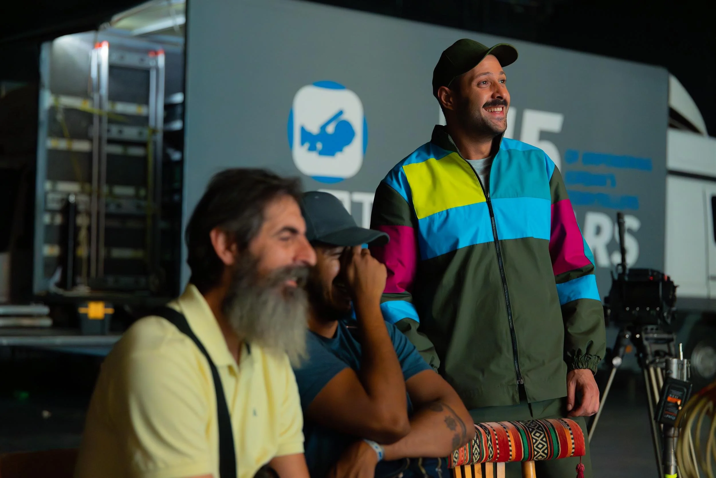Ahlan Simsim unit still: three crew members laugh together in front of a production truck.
