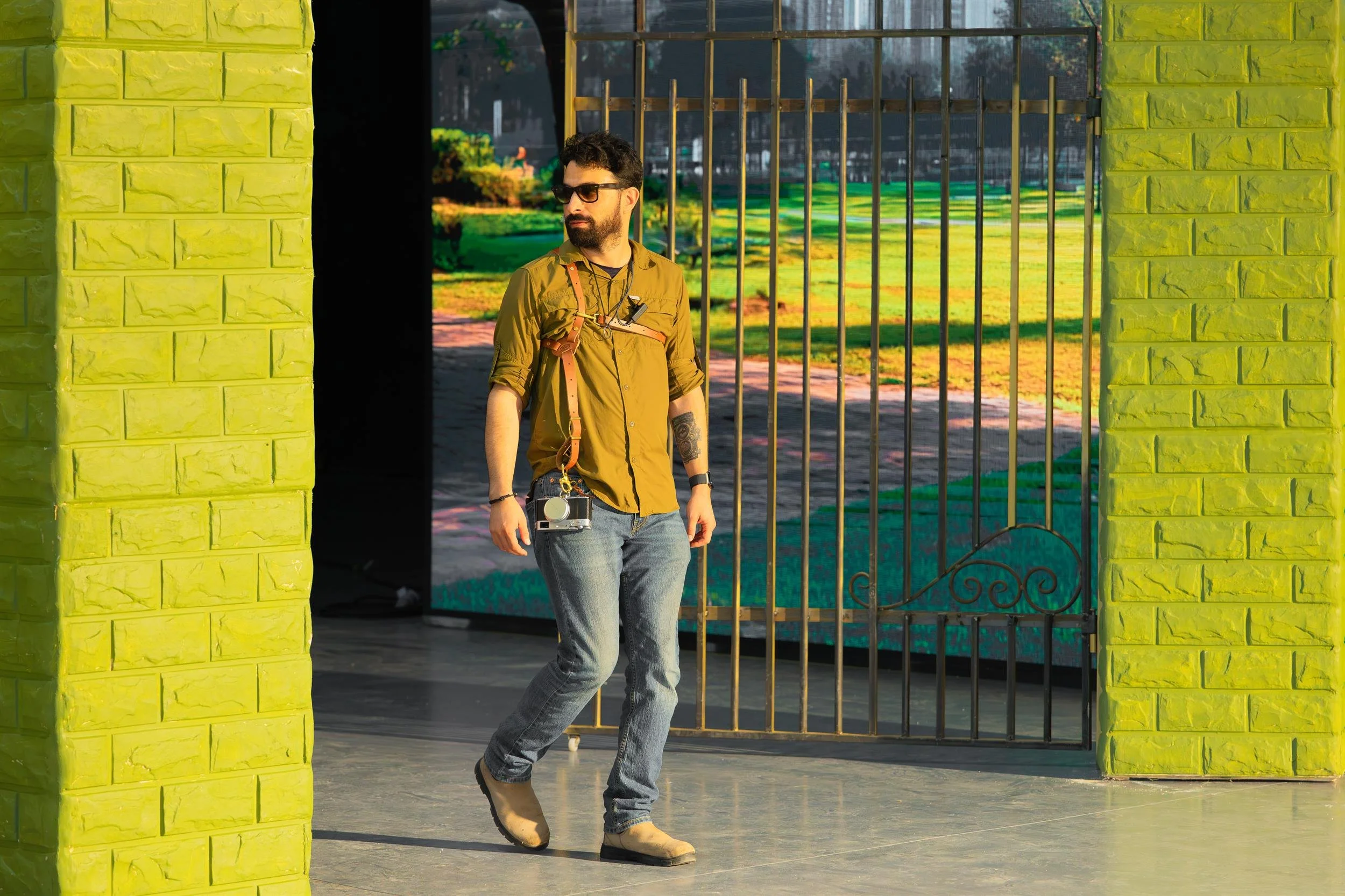 Ahlan Simsim unit still: A crew member wearing a camera harness walks between lime-green brick pillars on the studio set.