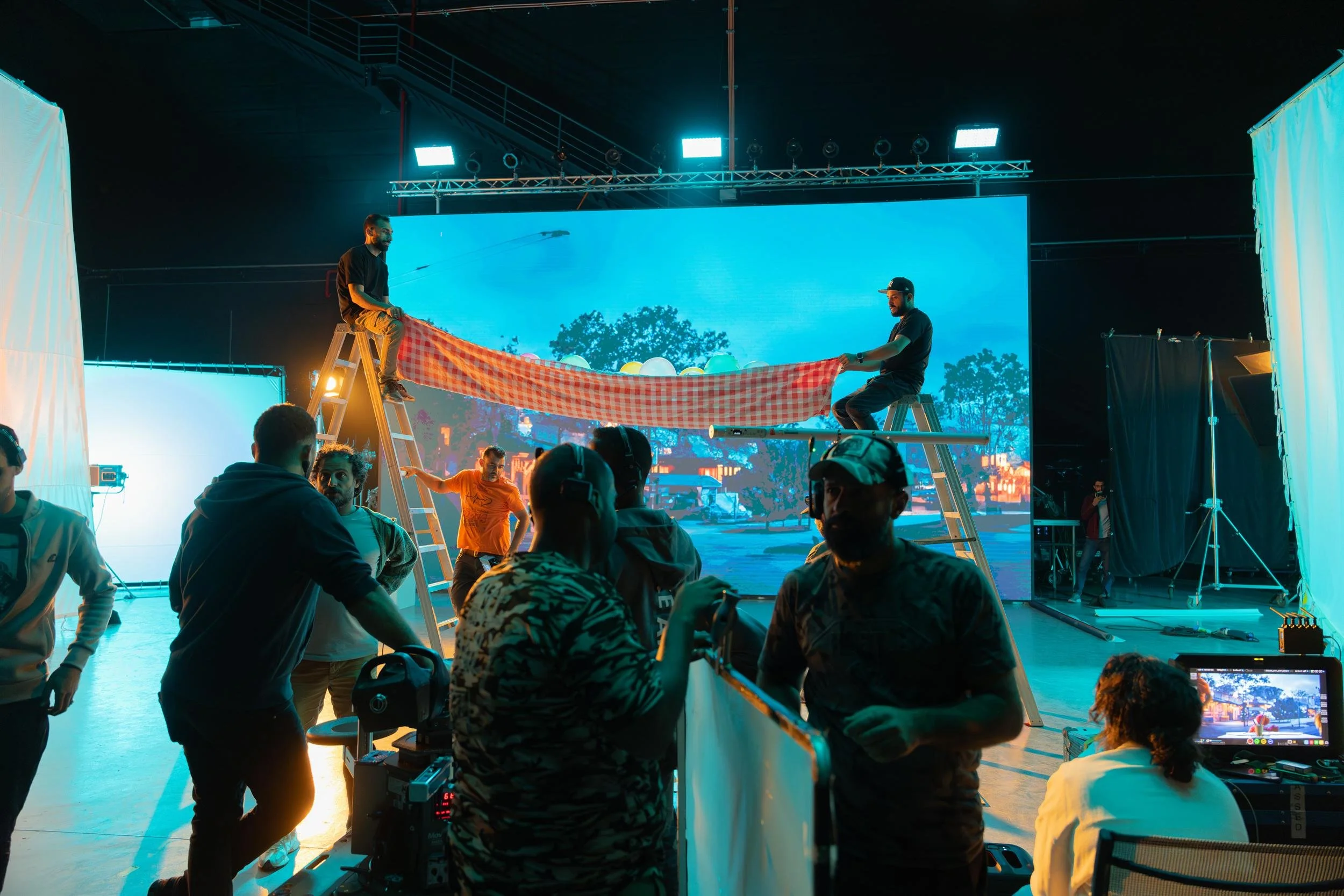 Ahlan Simsim unit still: crew on stepladders hold a red-and-white checkered banner in front of an LED dusk backdrop.