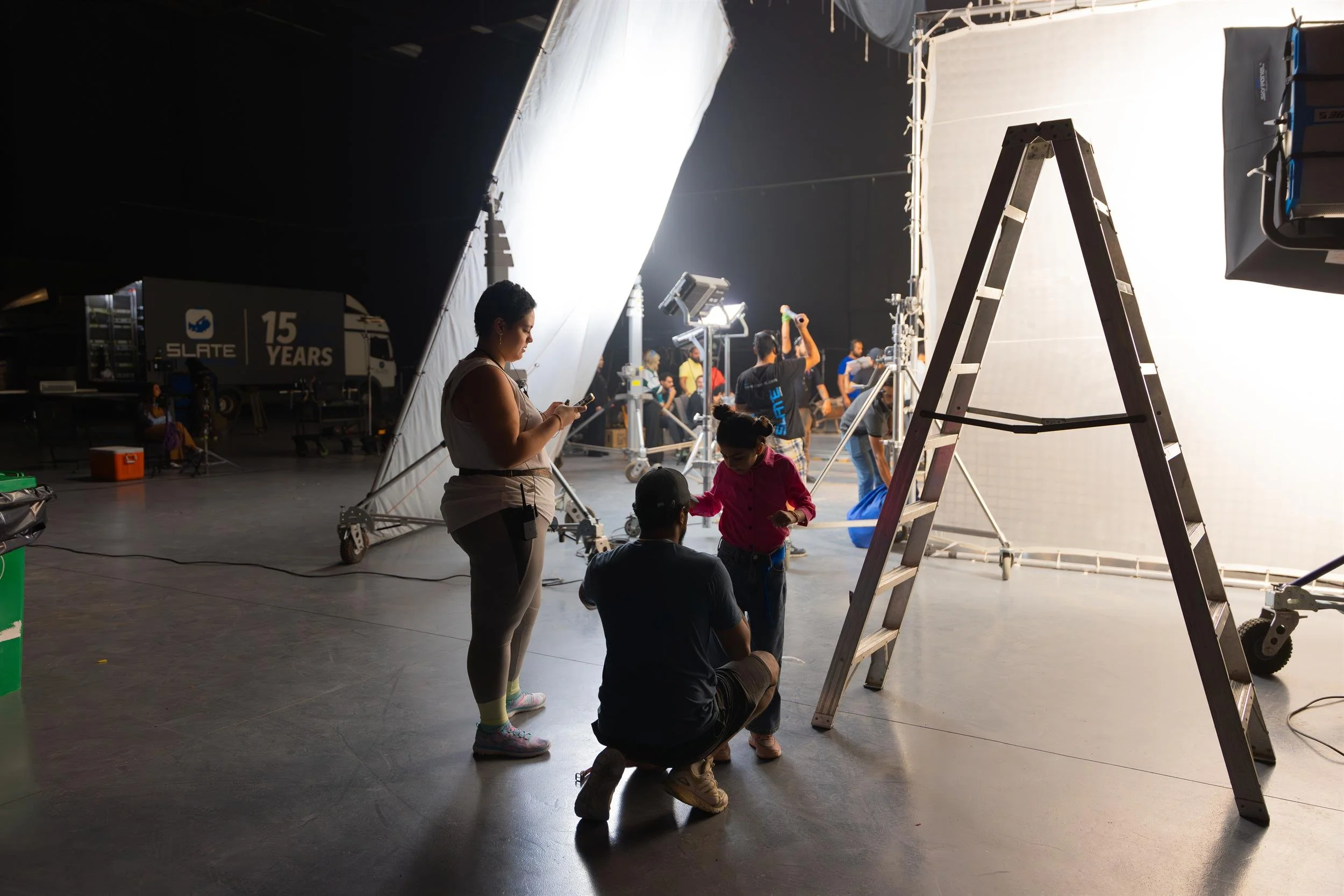 Ahlan Simsim unit still: Crew members work with a young girl on a studio set between large diffusion screens.