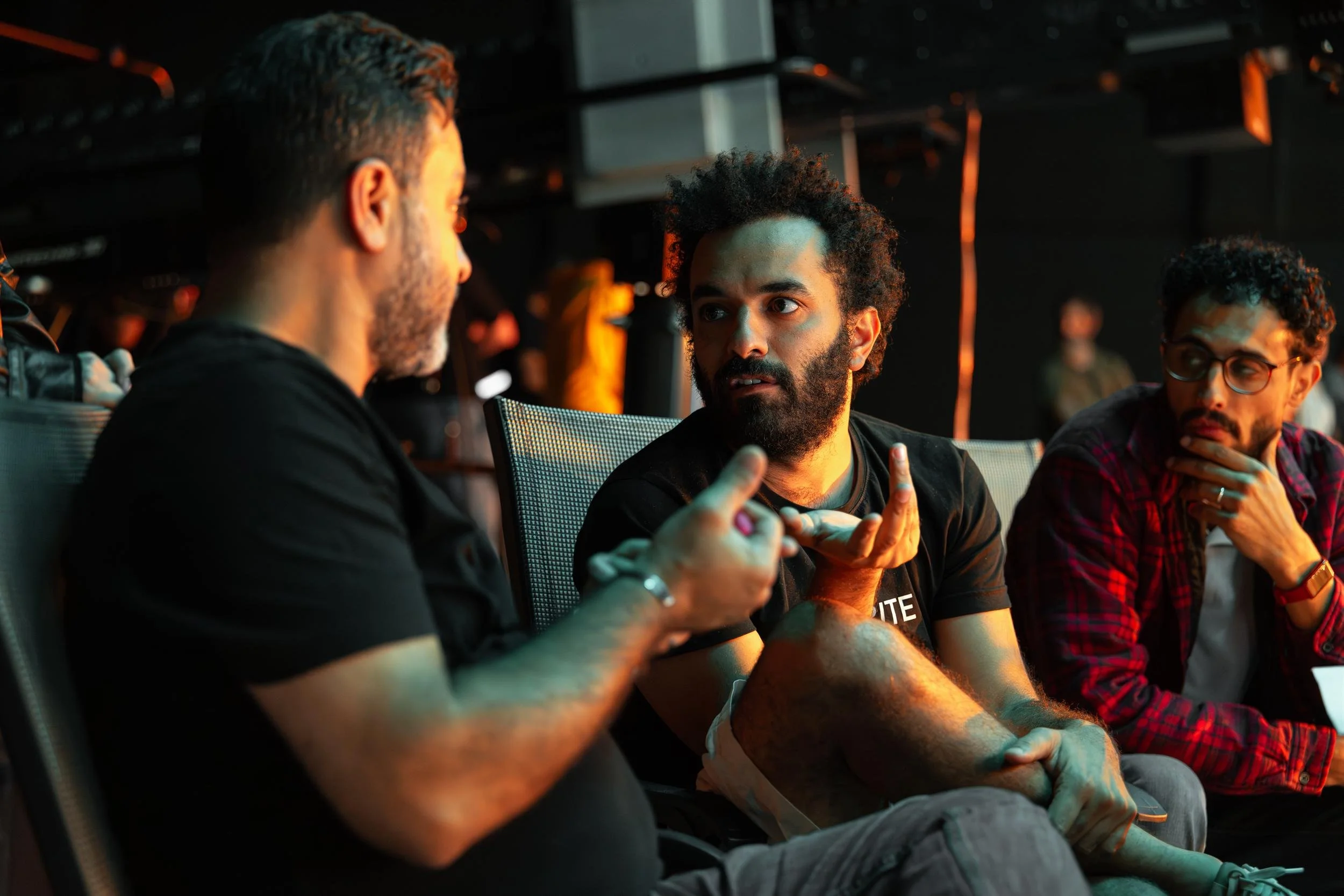 Ahlan Simsim unit still: three crew members sit in a dark studio talking under orange and teal light.