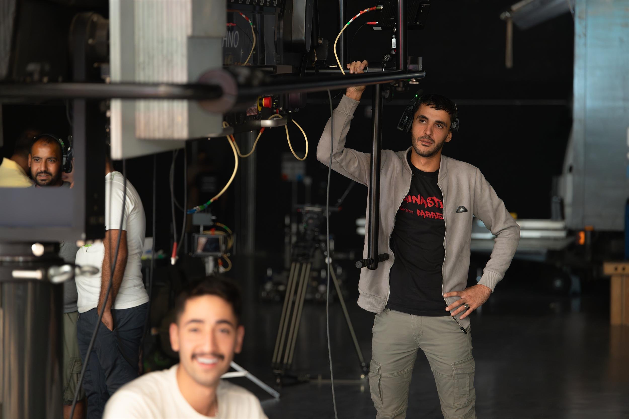Ahlan Simsim unit still: A crew member in headphones stands beside a large camera crane in a dark studio.