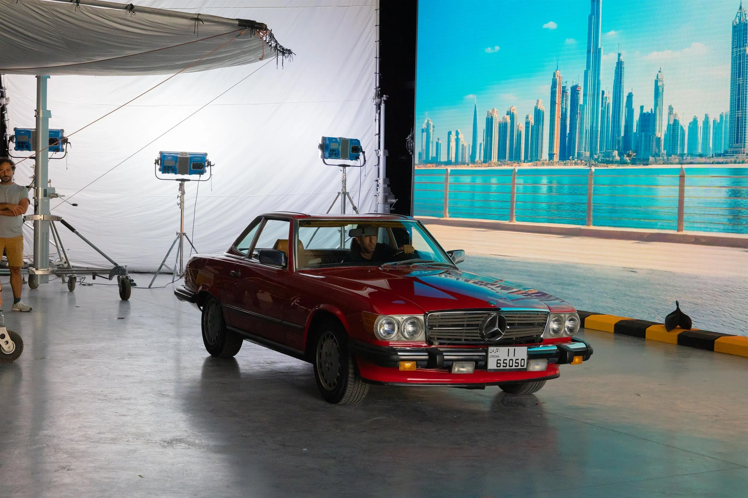 Ahlan Simsim unit still: a vintage red car sits on a studio floor before an LED city skyline, with lights and a crew member nearby.