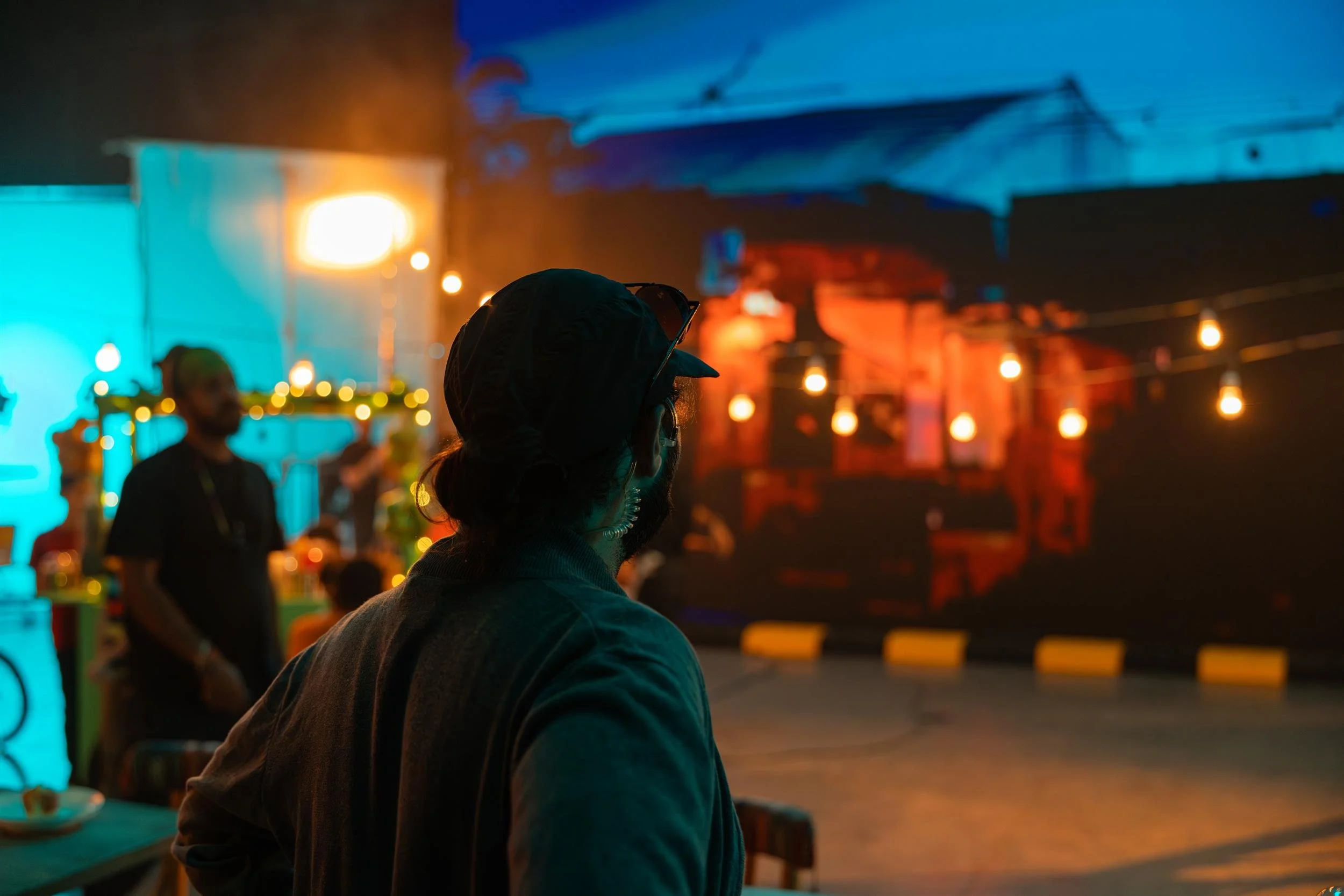 Ahlan Simsim unit still: a crew member watches a night set decorated with warm string lights.