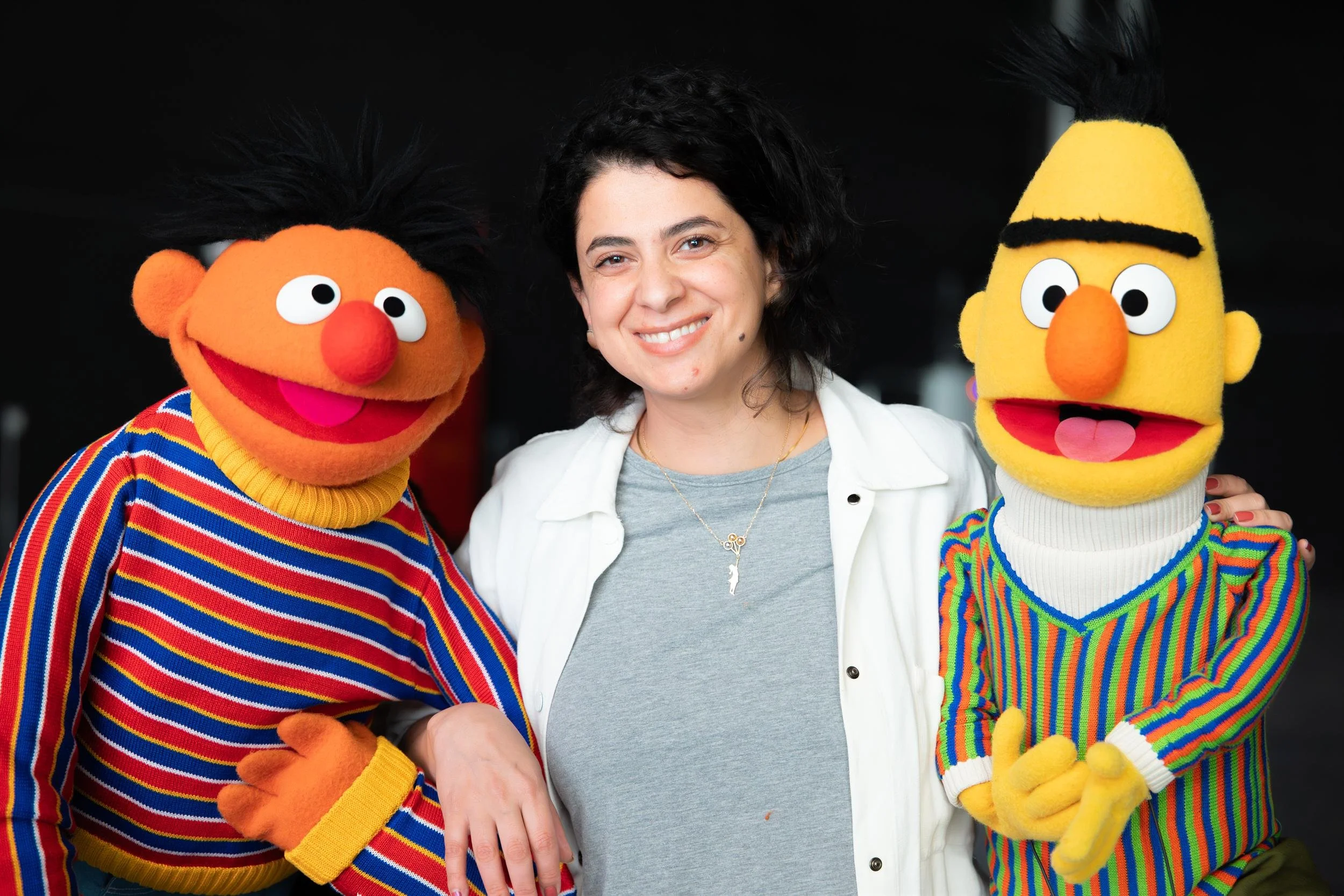 Ahlan Simsim unit still: a woman smiles while posing between Ernie and Bert.