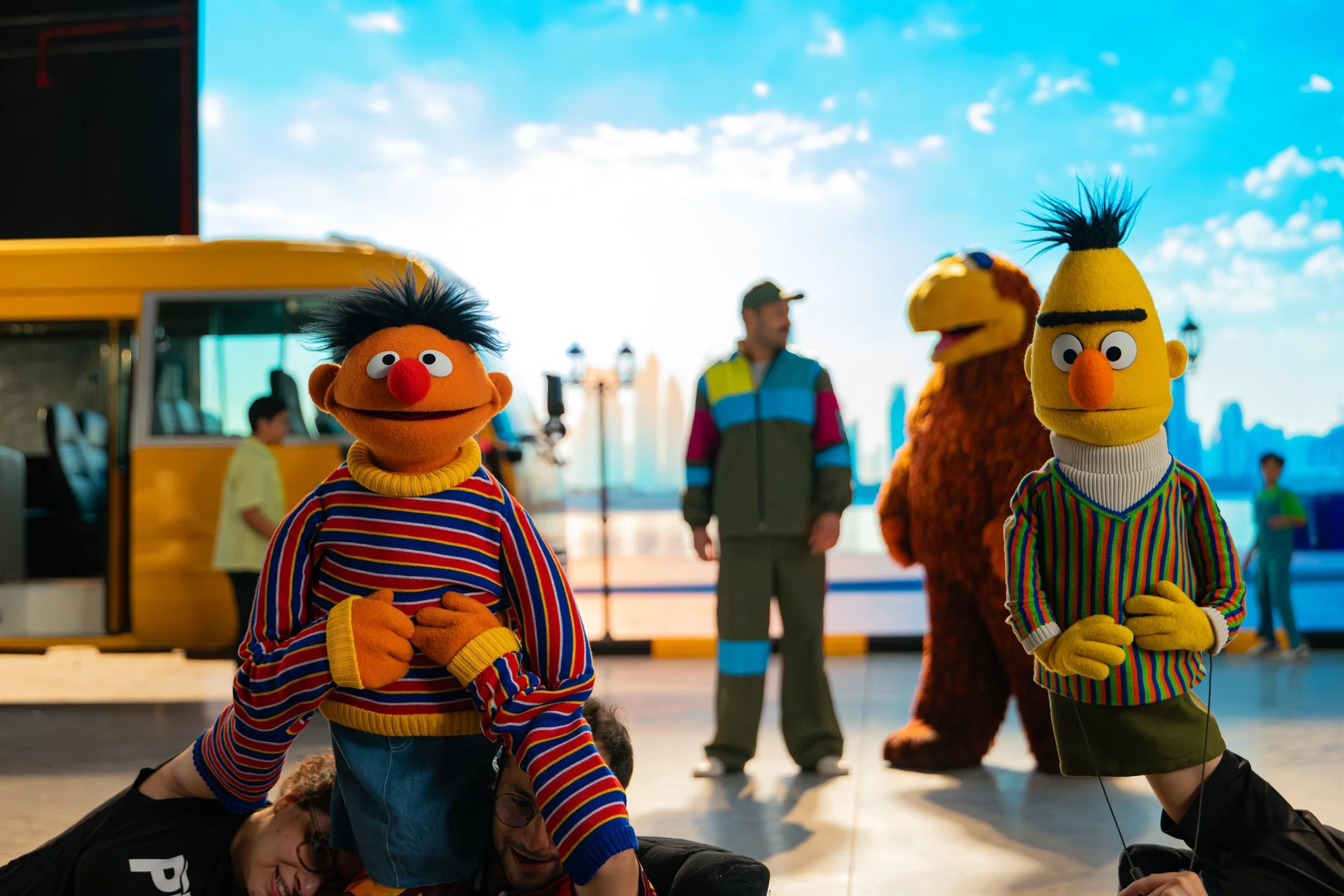 Ahlan Simsim unit still of Ernie and Bert with puppeteers and crew beside the school bus set