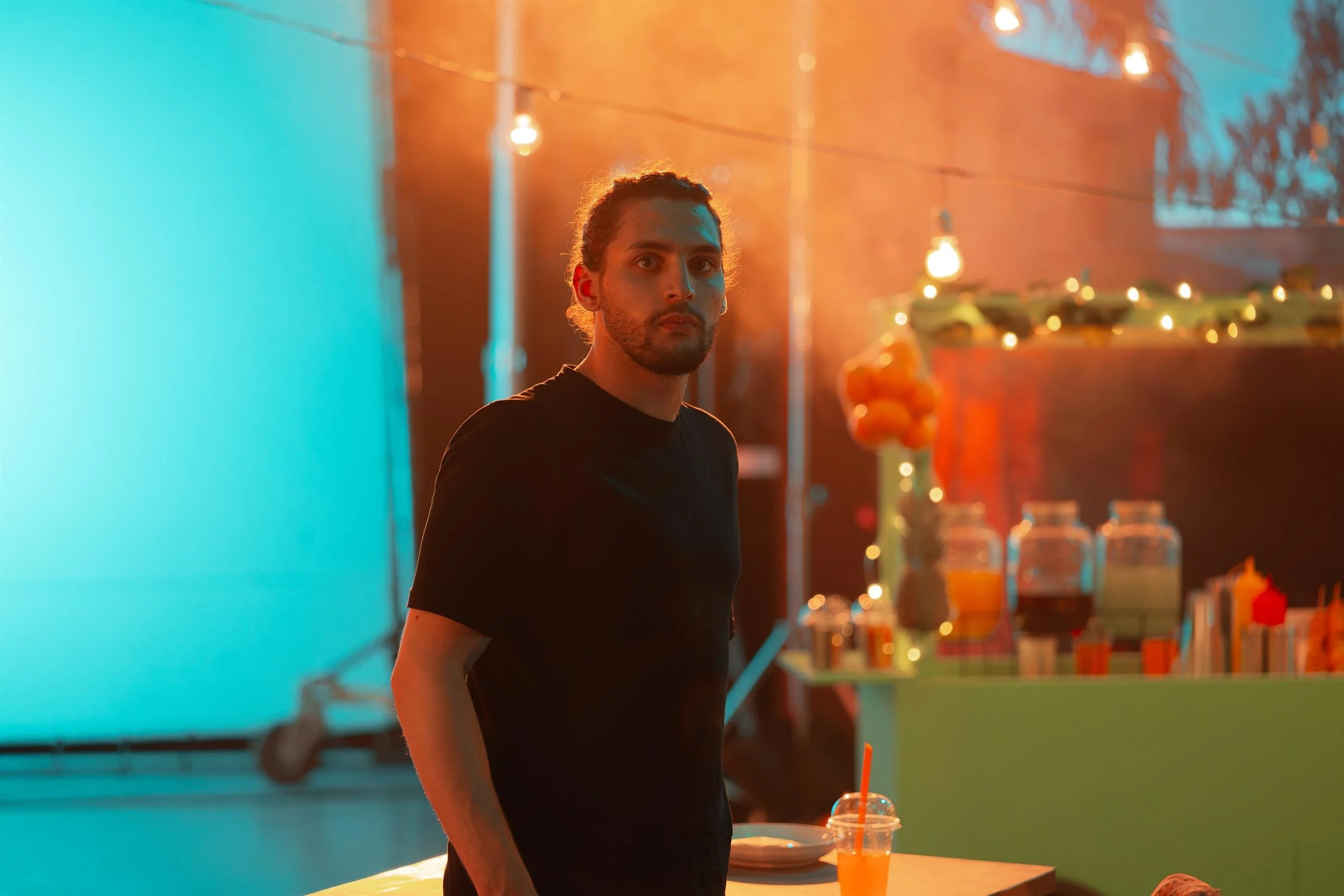 Behind the scenes: crew member standing on the lit market set at night, string lights and teal LED wall behind him