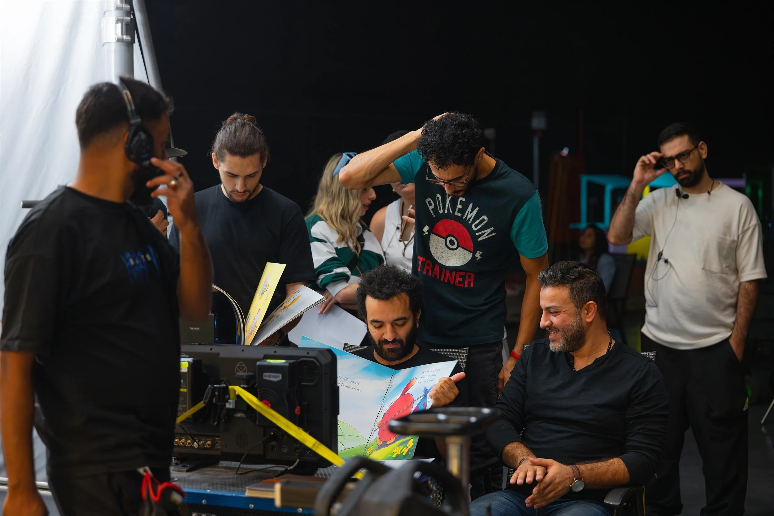 Ahlan Simsim unit still: Crew members gather around a production monitor and look at an illustrated children's book.