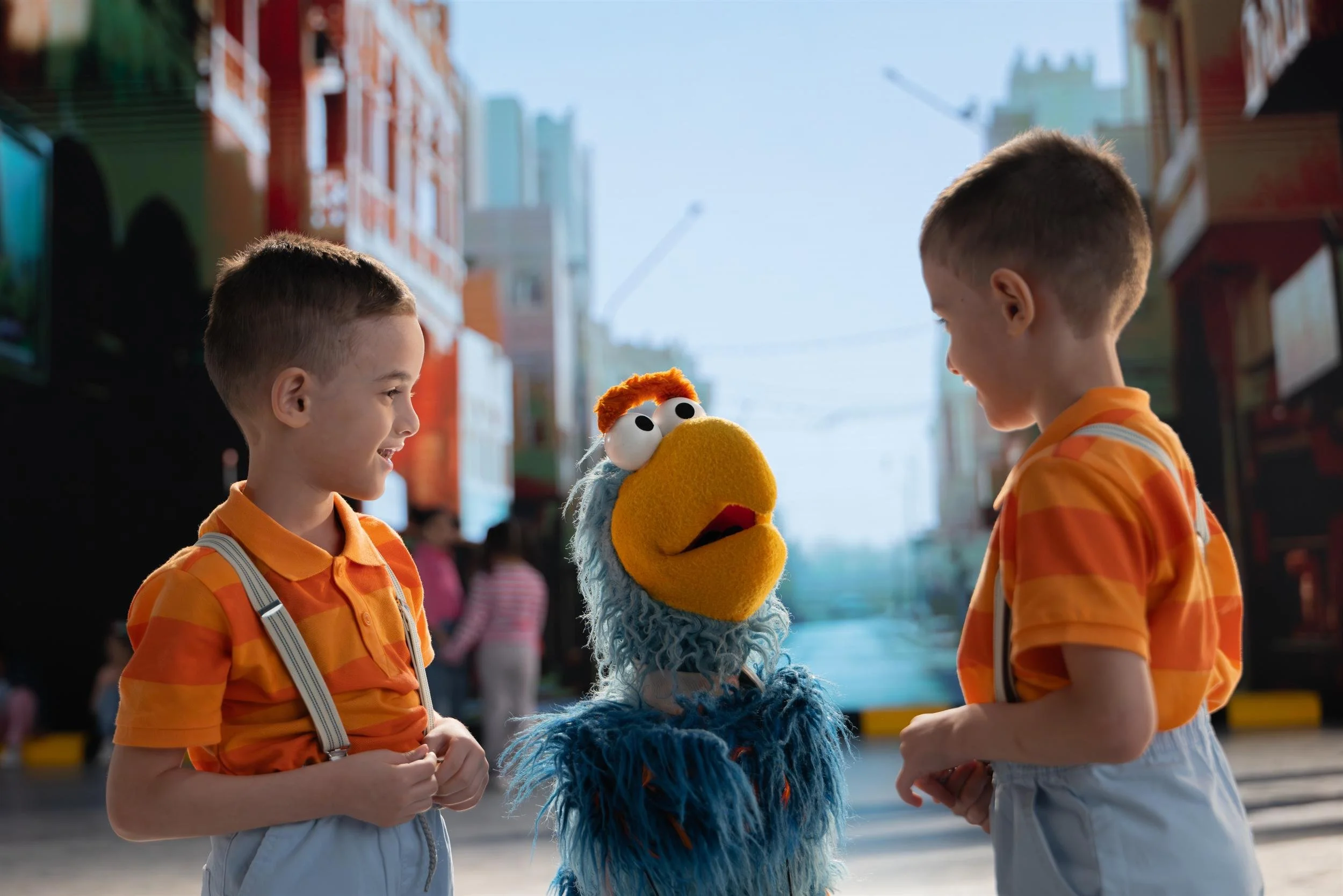 Ahlan Simsim key art: two boys face a teal muppet between them on the painted street set.