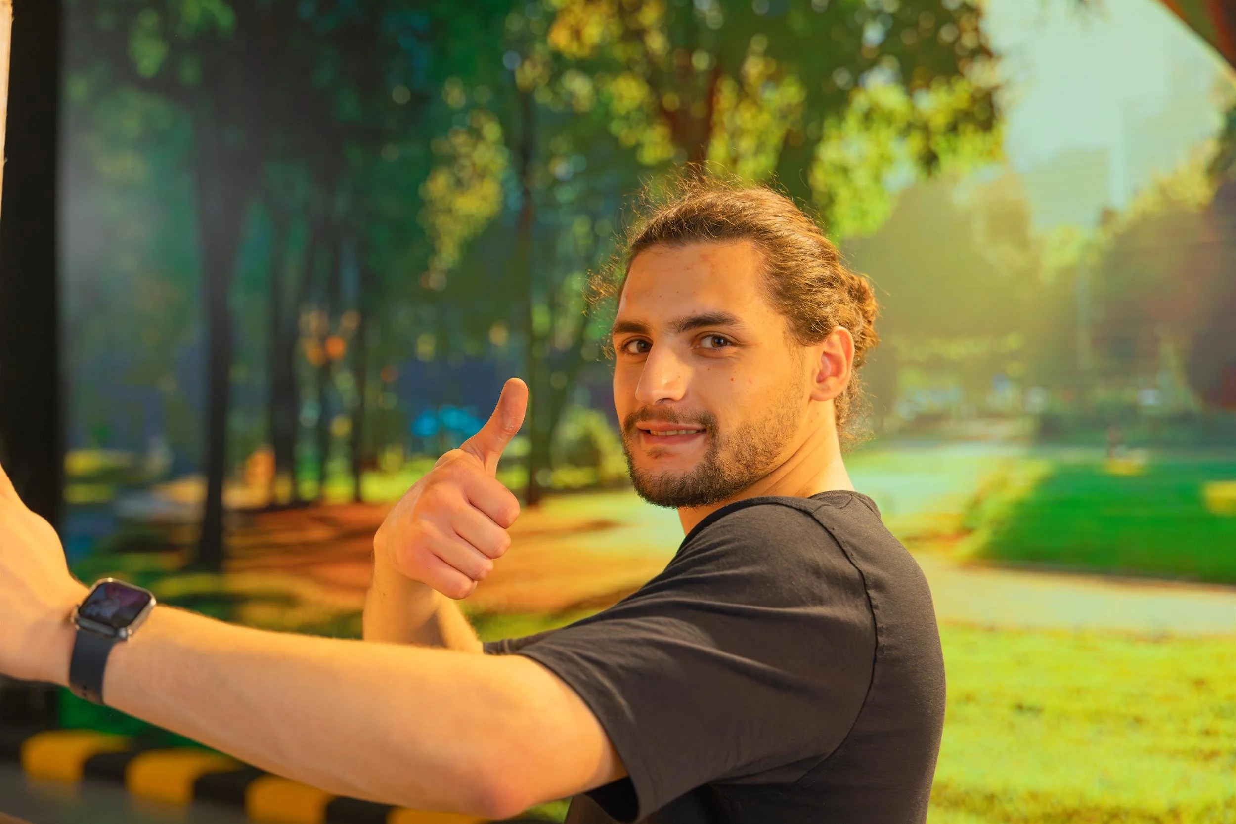 Ahlan Simsim unit still: A smiling crew member looks over his shoulder and gives a thumbs-up in front of a park backdrop.