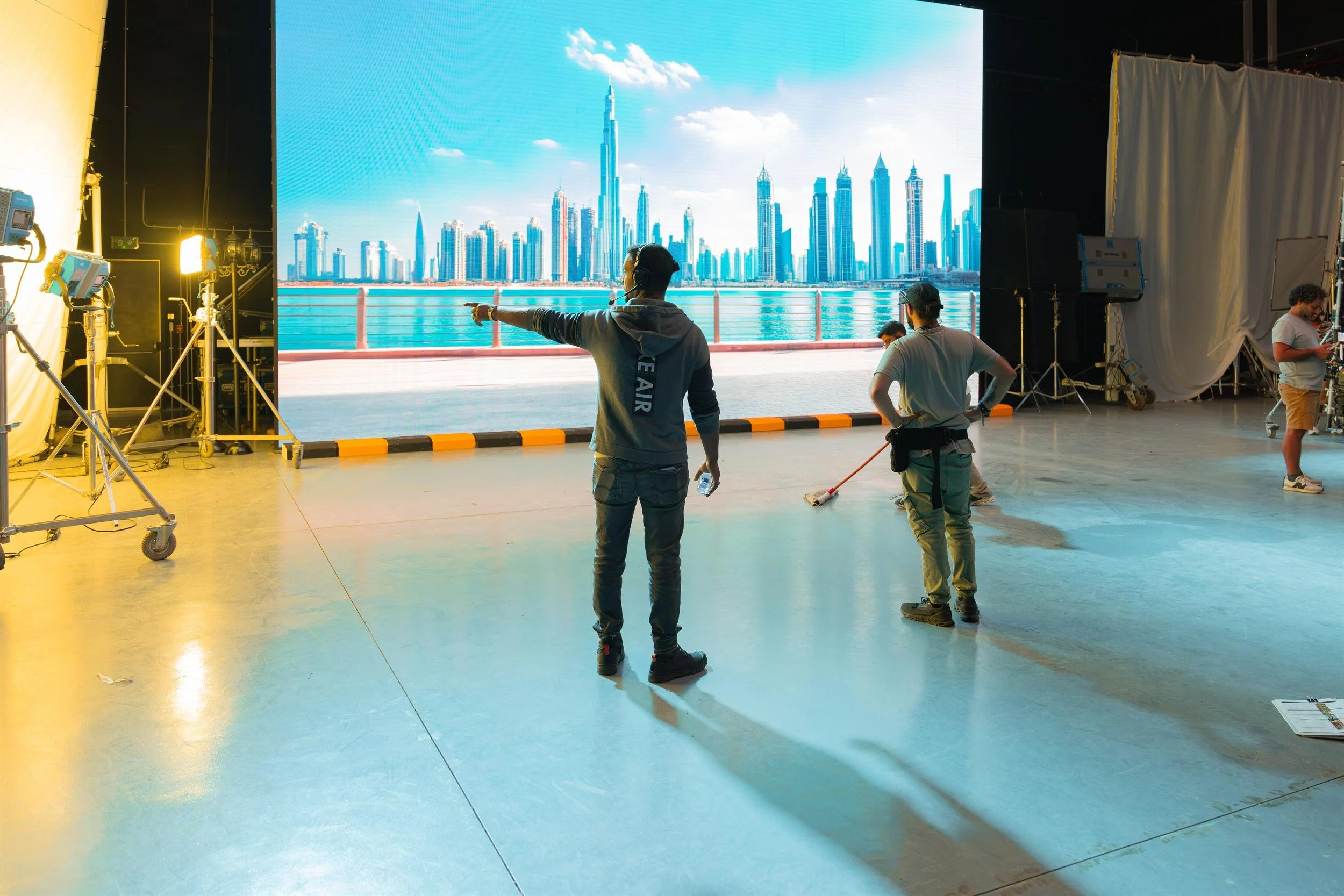 Ahlan Simsim unit still: three crew members face an LED wall showing a city skyline over water.