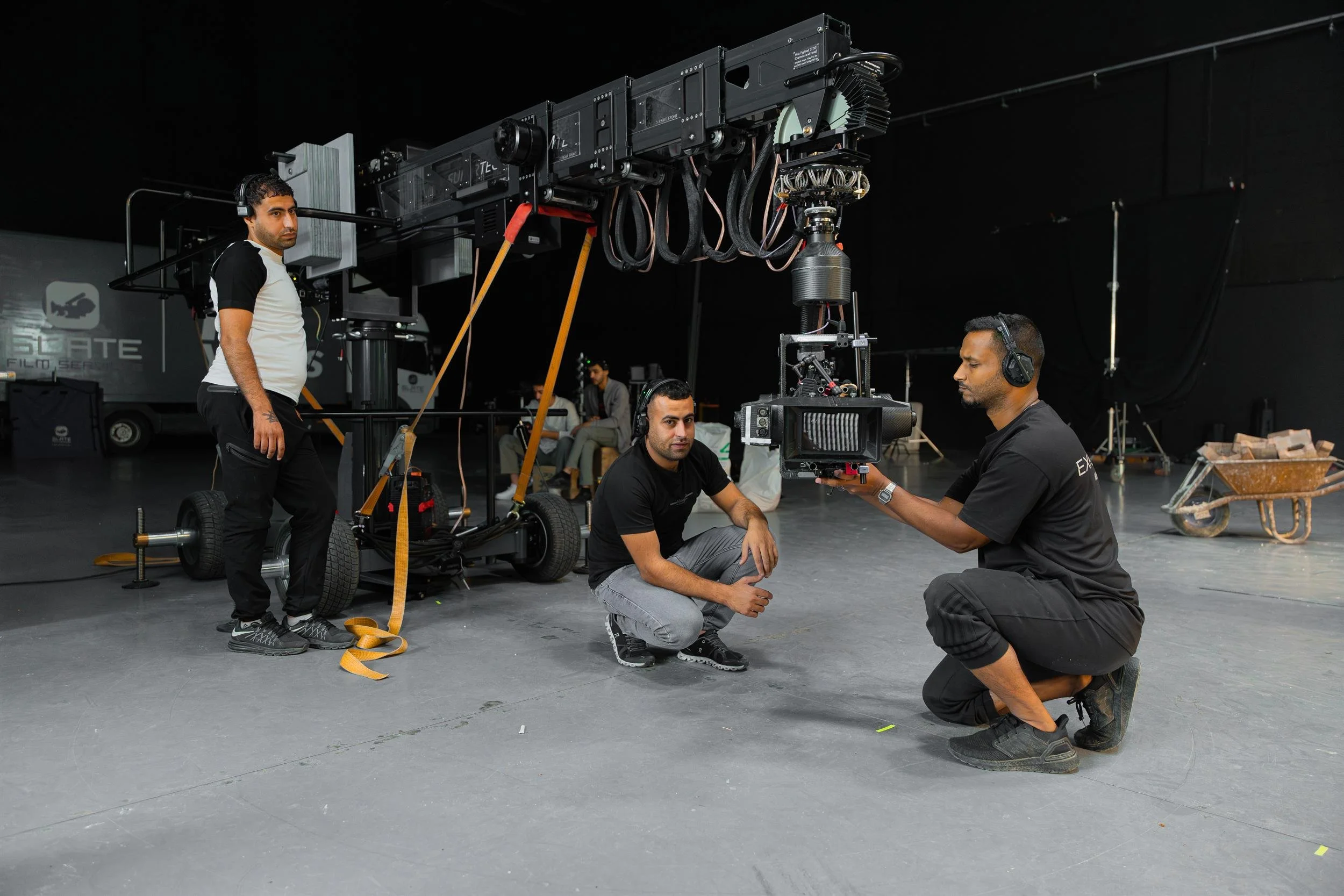 Ahlan Simsim unit still: Three crew members in headsets work with a large camera crane in a dark film studio.