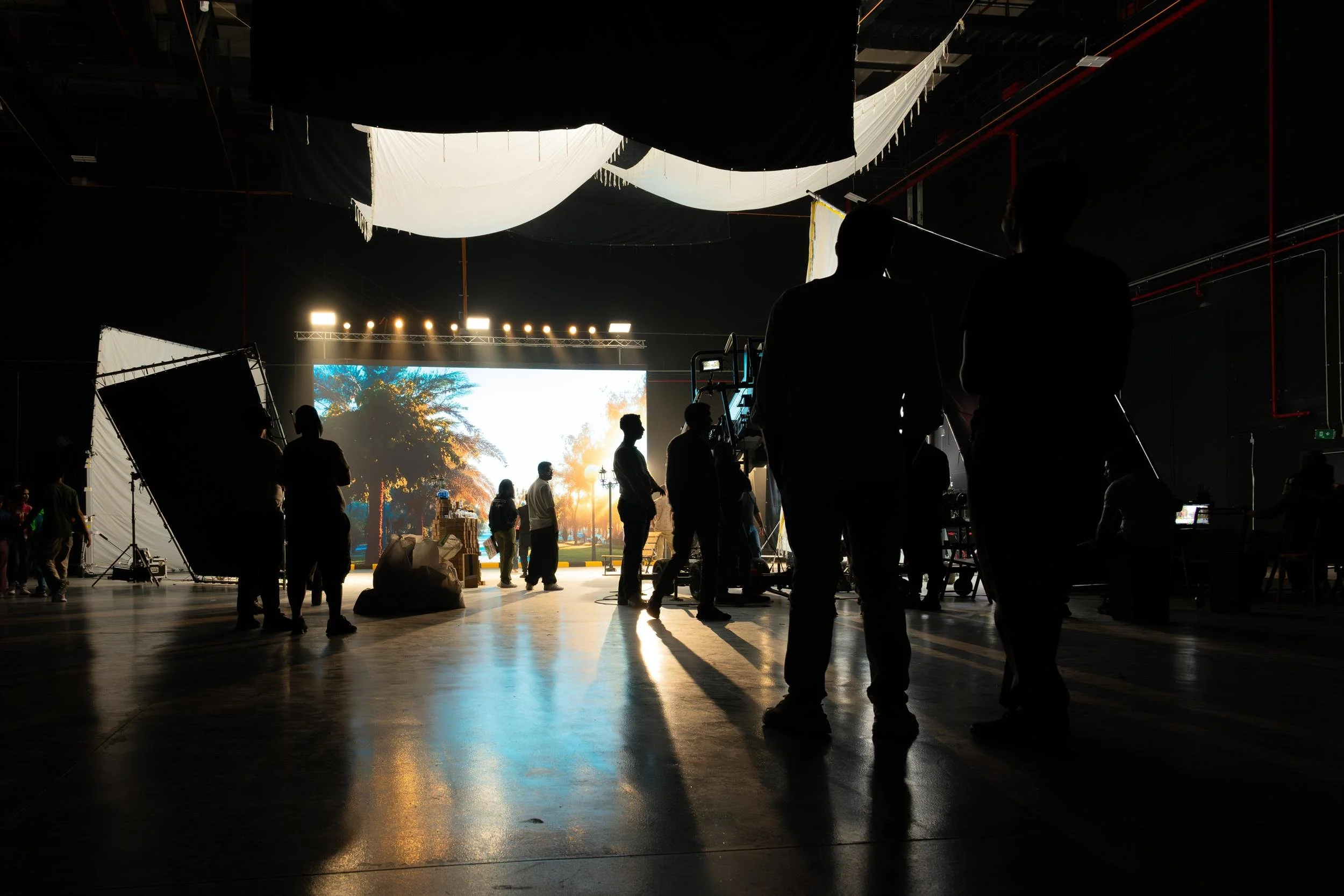 Ahlan Simsim unit still: crew silhouettes stand against an LED park sunset in a dark studio.