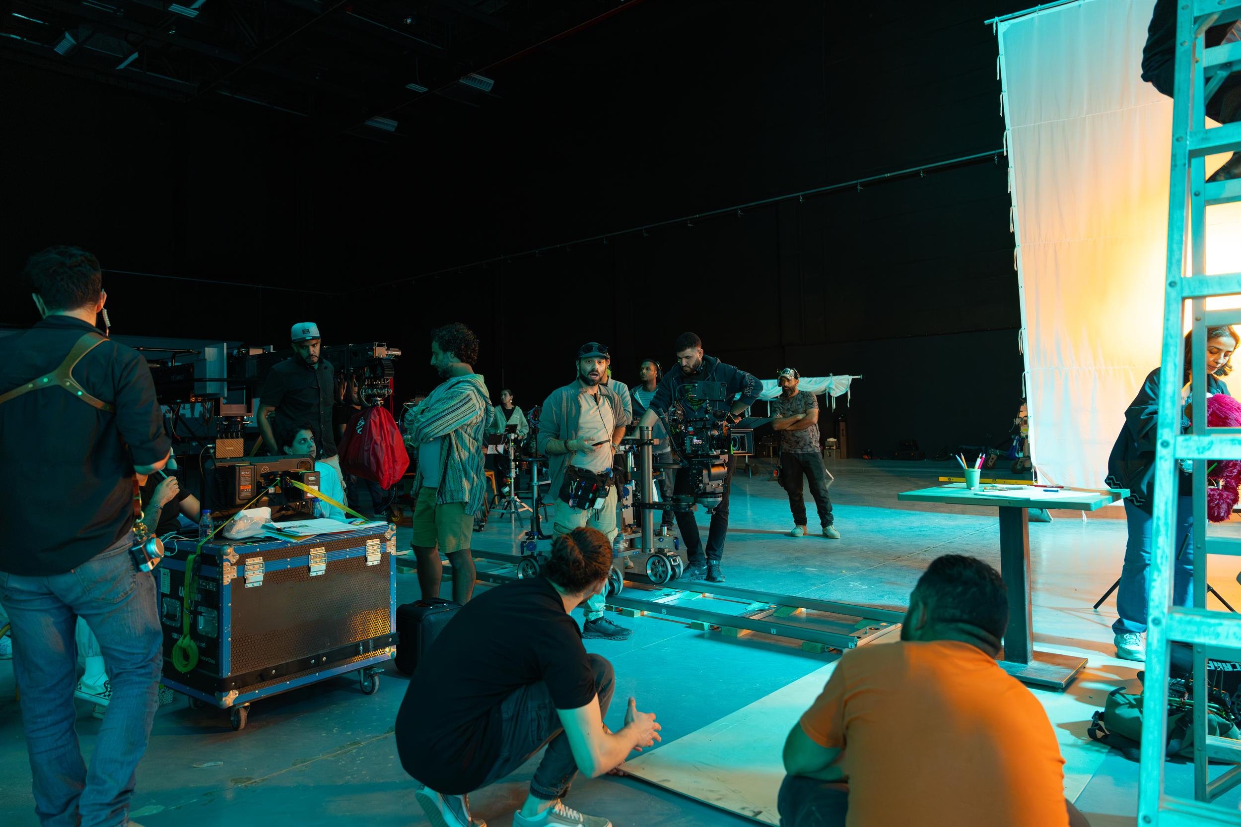 Ahlan Simsim unit still: crew prepare a camera on dolly tracks beside an orange-lit diffusion screen.