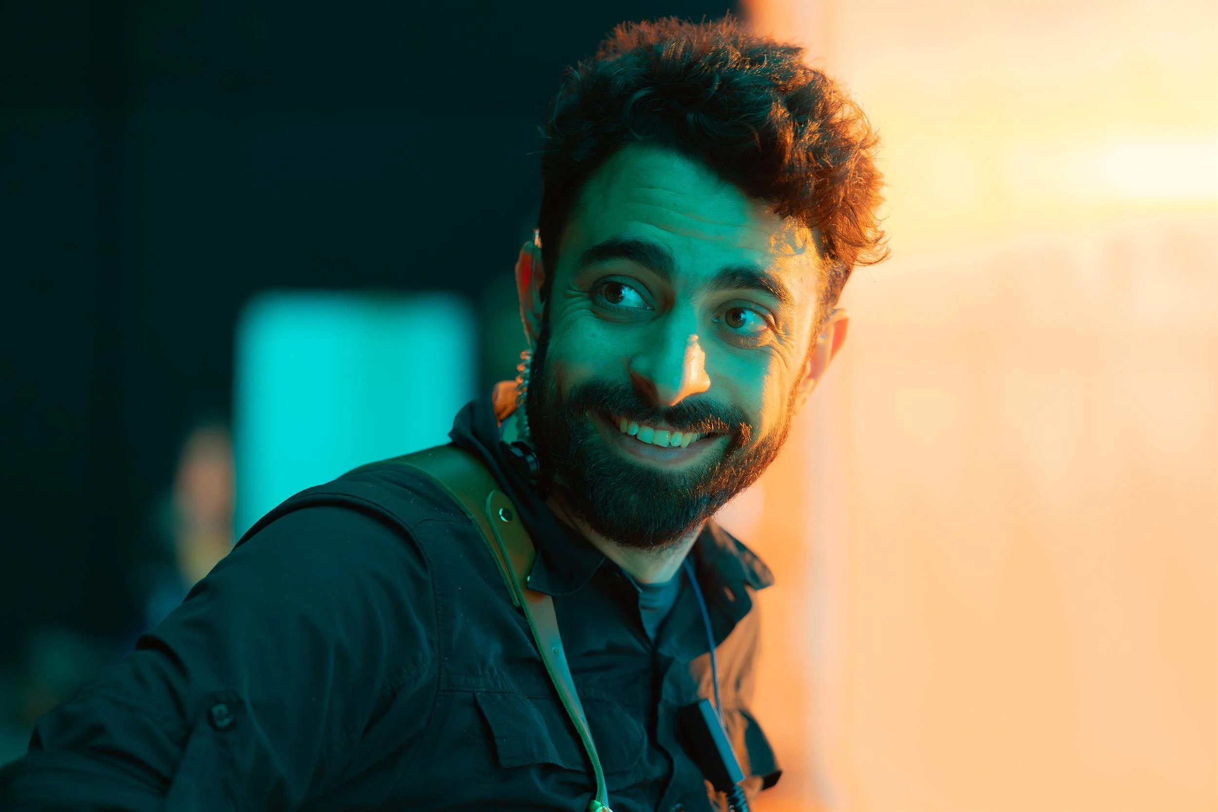Ahlan Simsim unit still: a smiling crew member with a headset under teal and orange lighting.