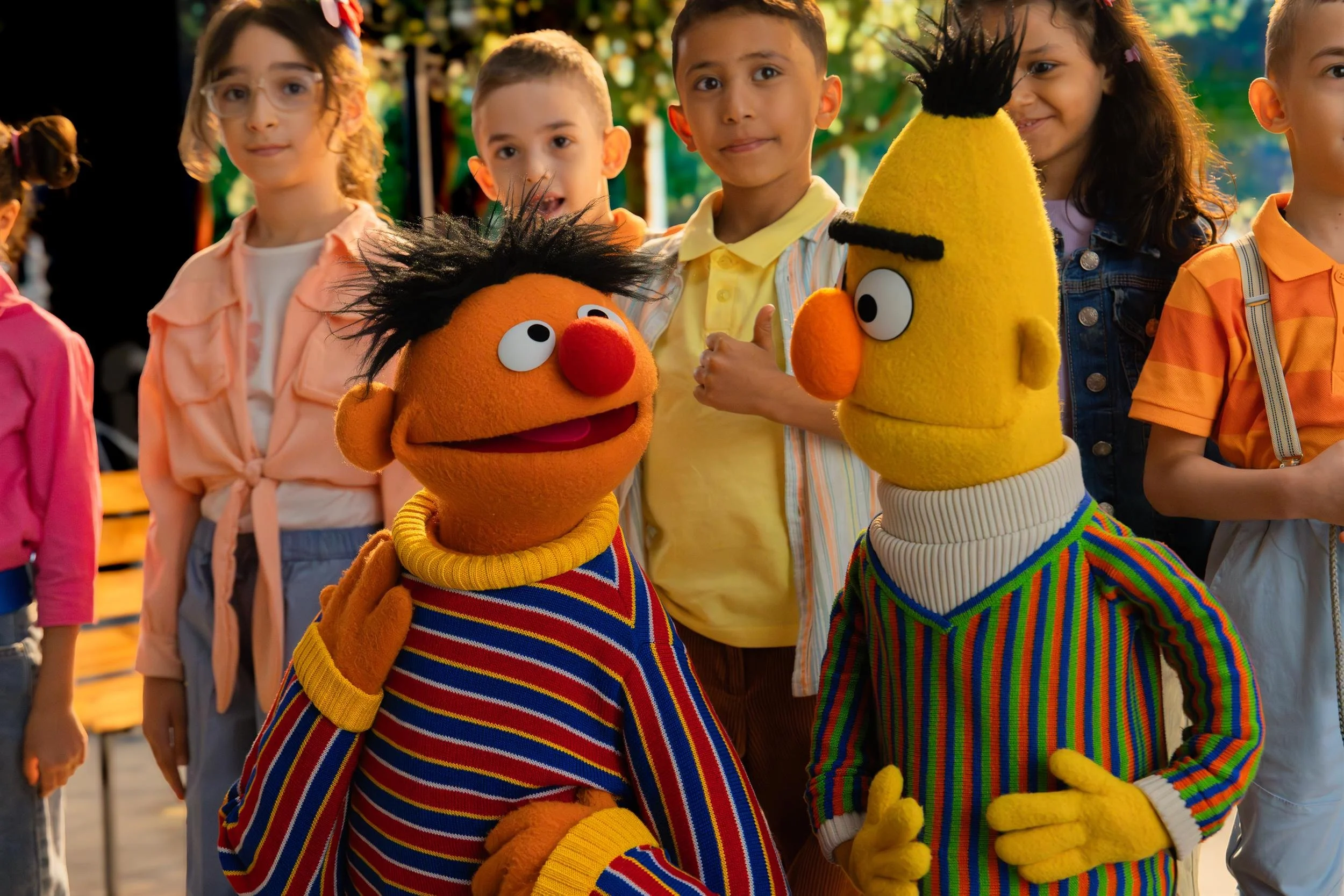 Ahlan Simsim unit still: Ernie and Bert stand with a group of children on a colorful outdoor park set.