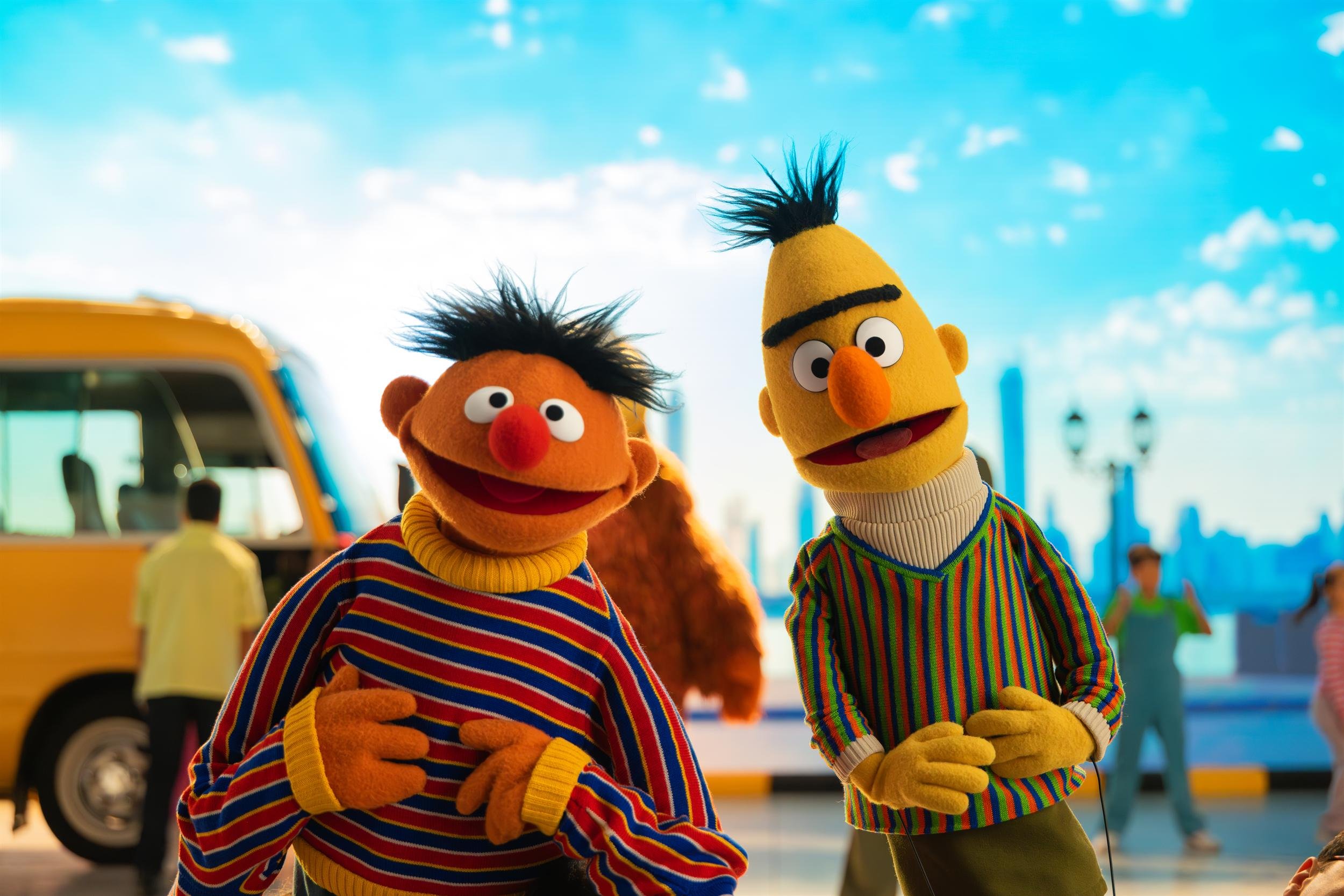 Ahlan Simsim key art: Ernie and Bert stand in front of a yellow bus with a painted city backdrop.