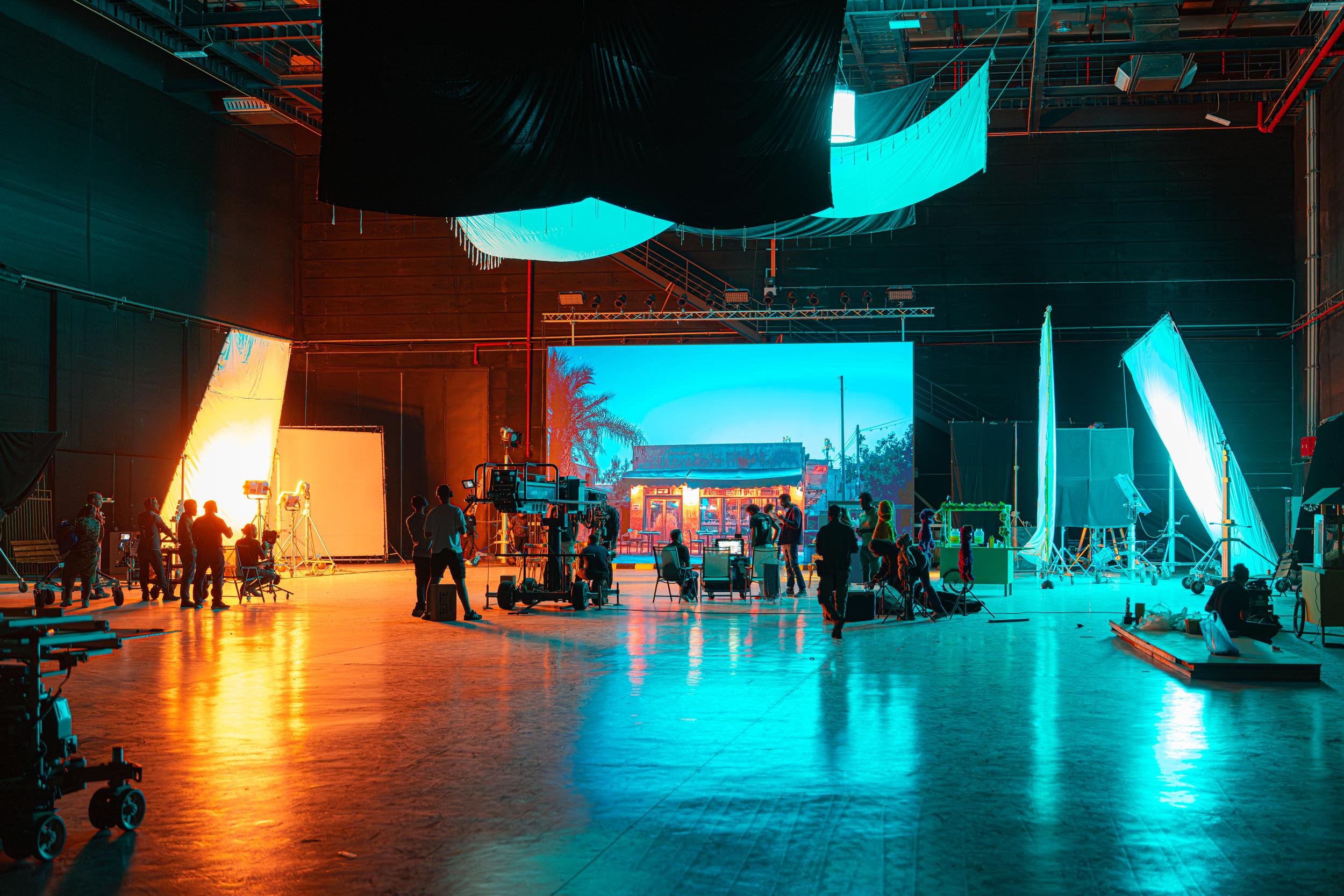 Ahlan Simsim unit still: a wide studio view of an LED street backdrop, camera dolly, and crew silhouettes.