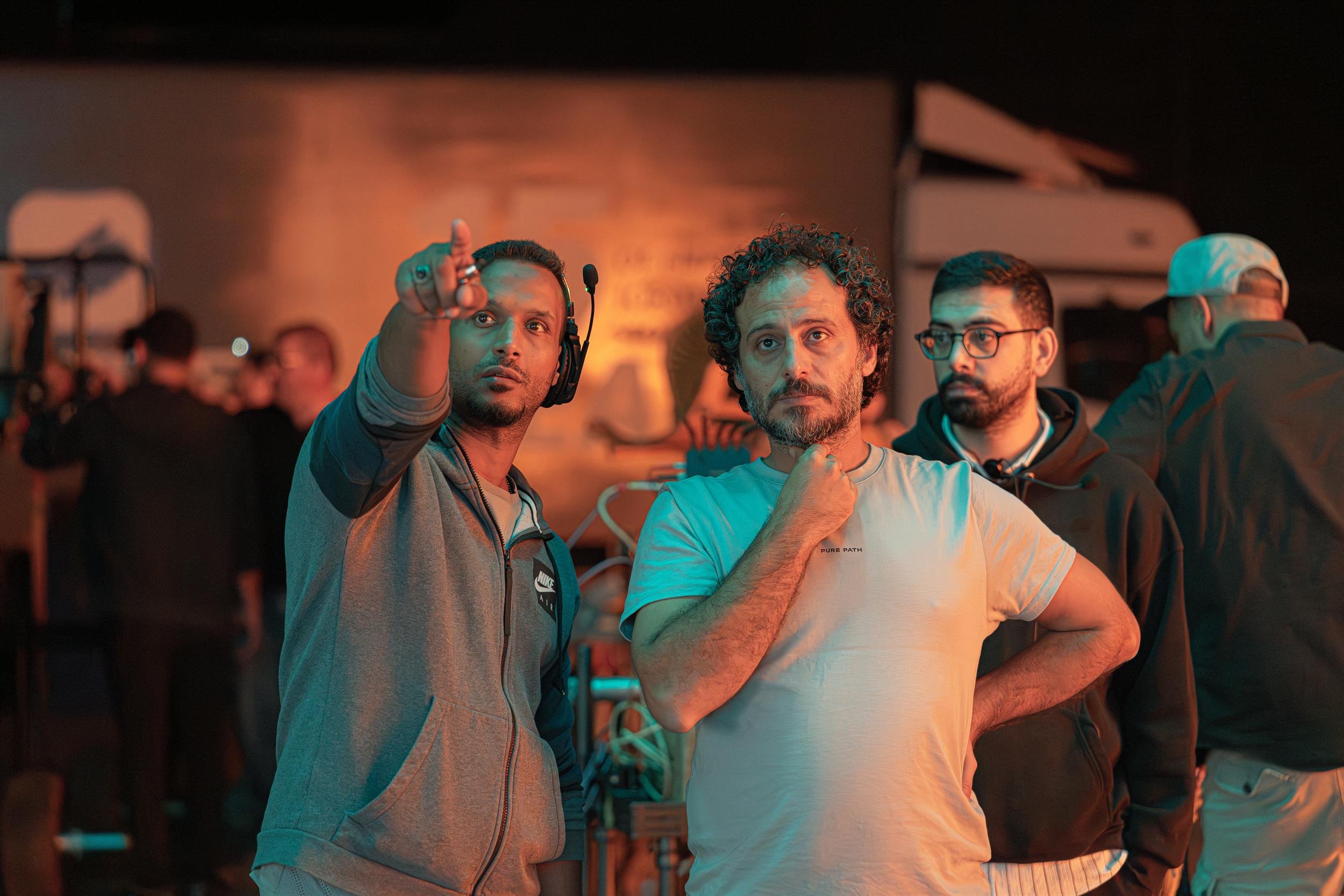 Ahlan Simsim unit still: three crew members look off-camera, one pointing, on a dimly lit set.