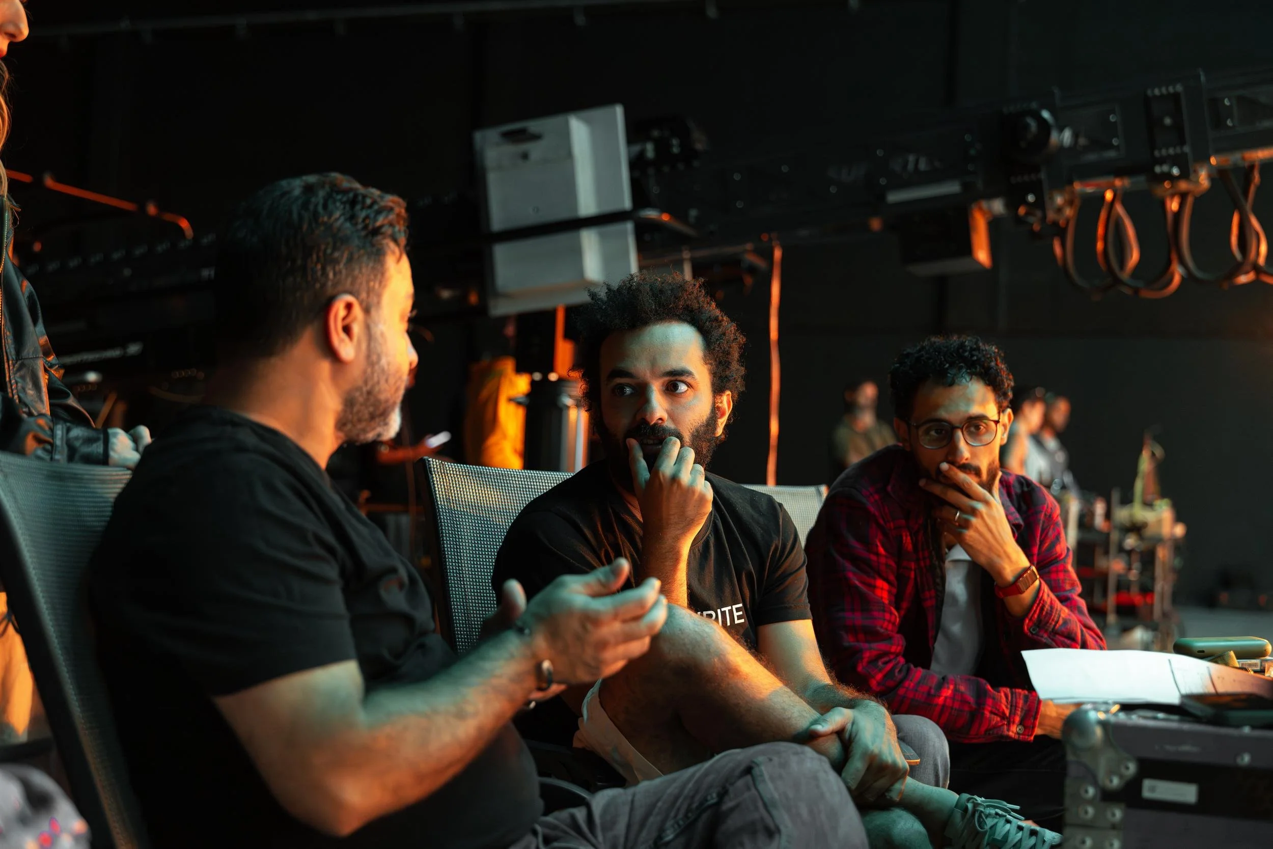 Ahlan Simsim unit still: three crew members sit in mesh chairs on a dark set beneath a camera crane.