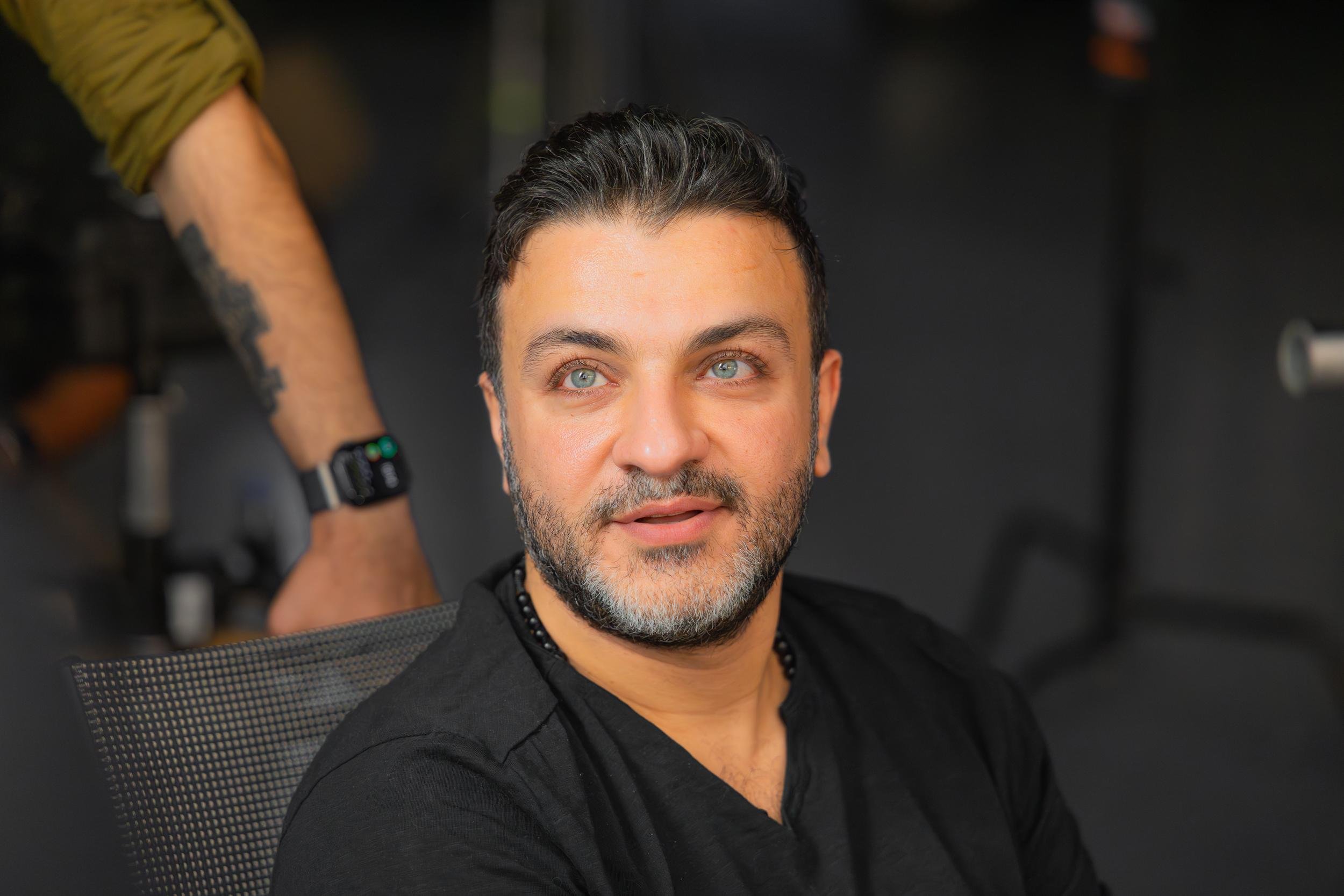 Ahlan Simsim unit still: A man with a beard and light eyes looks off-camera while sitting on set.