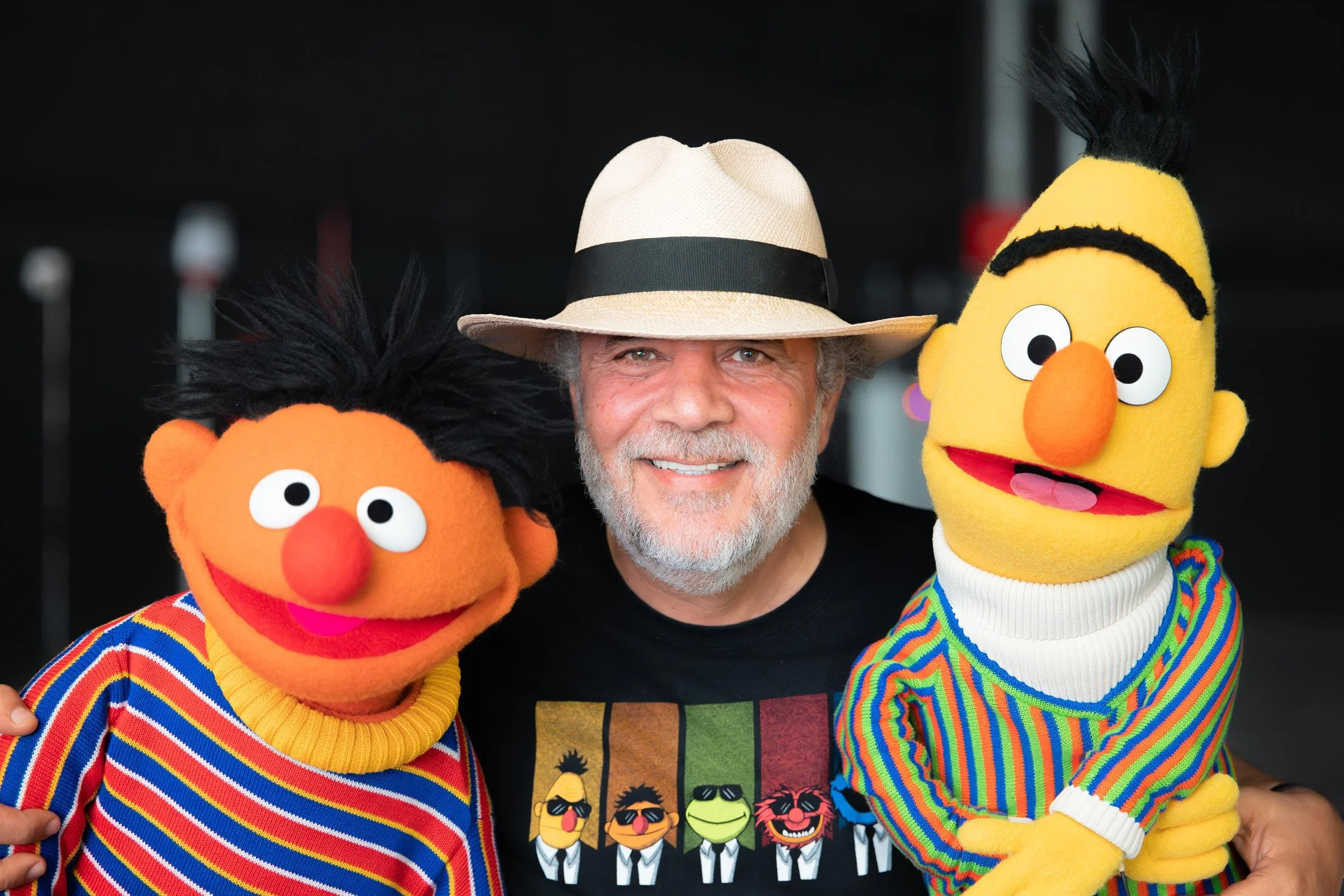Ahlan Simsim unit still: a smiling man in a straw hat poses with his arms around Ernie and Bert.