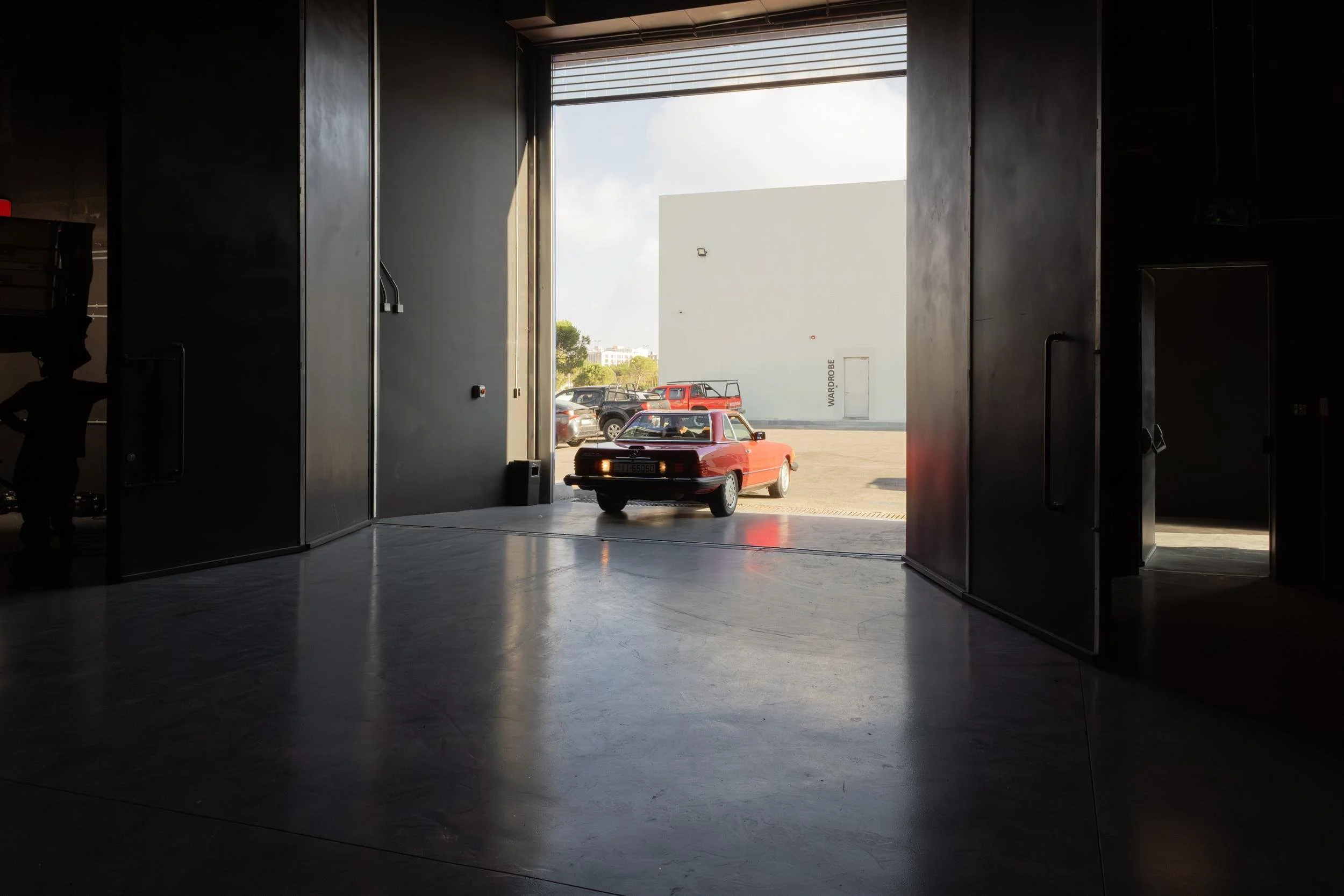 Ahlan Simsim unit still: View from inside a dark studio looking out at a red car parked near a wardrobe building.