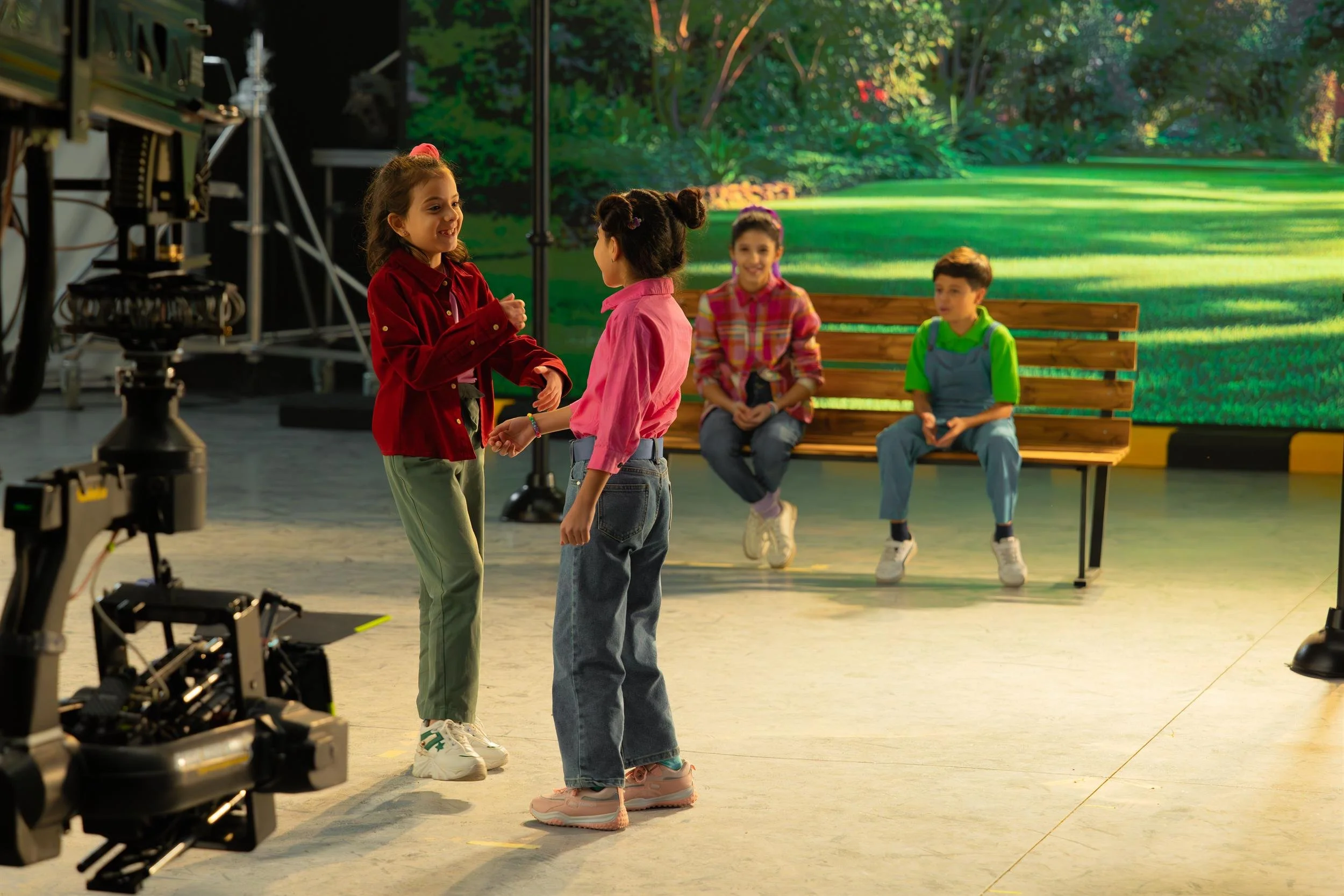 Ahlan Simsim unit still: four children on a park set with a camera crane and LED backdrop.