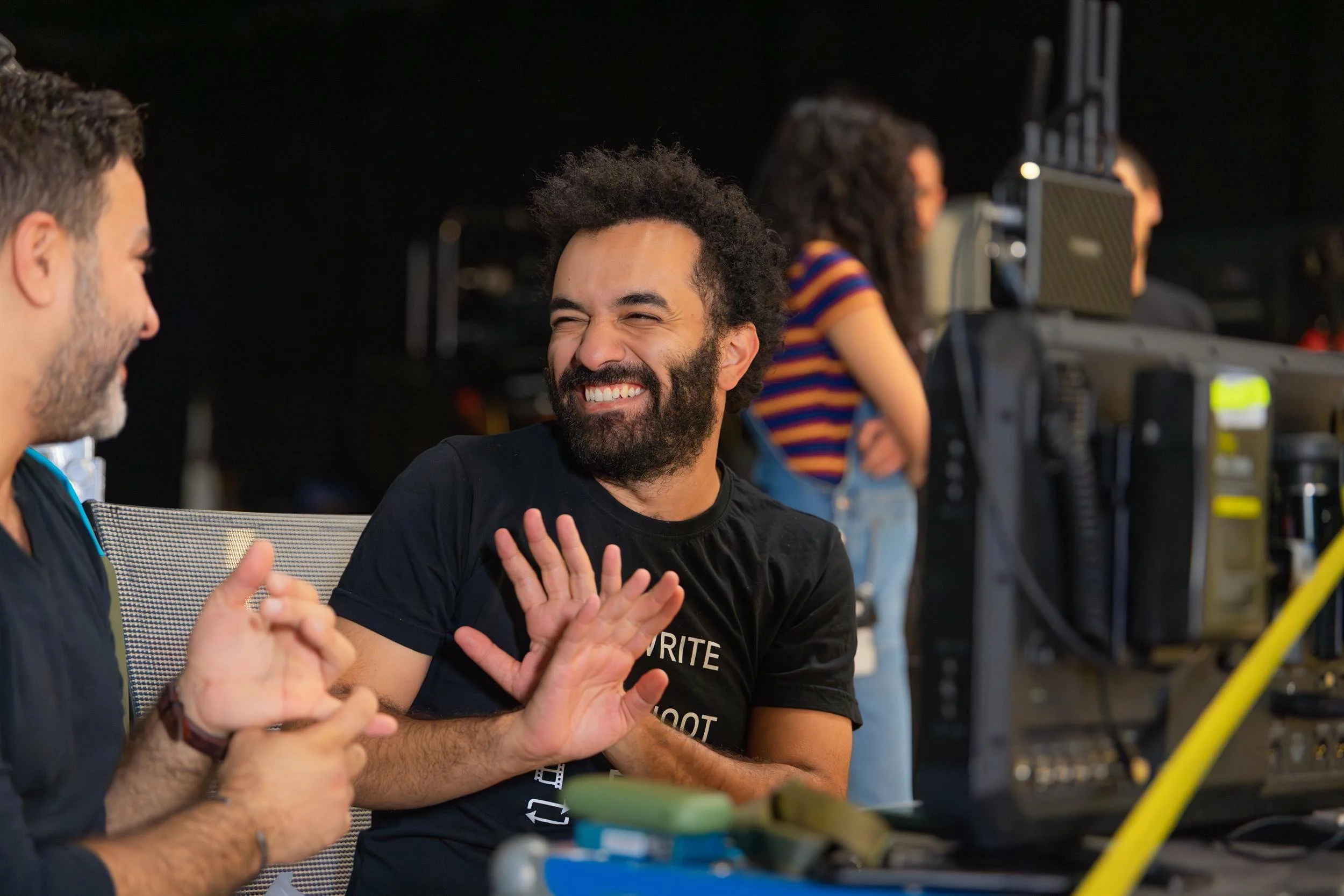 Ahlan Simsim unit still: A bearded crew member laughs and gestures playfully while talking with a colleague on set.