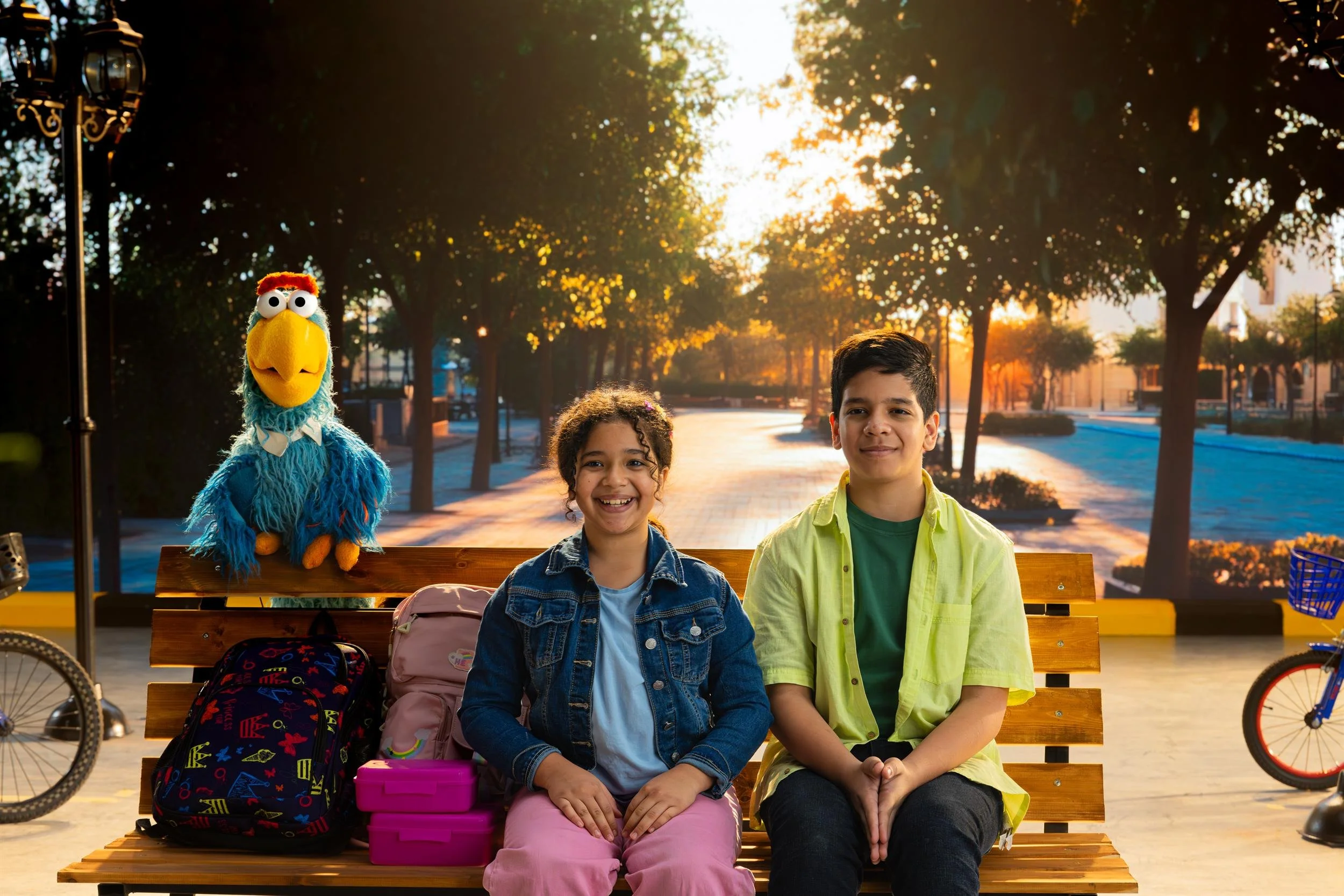 Ahlan Simsim key art: two children sit on a park bench between Bert and a blue bird muppet.