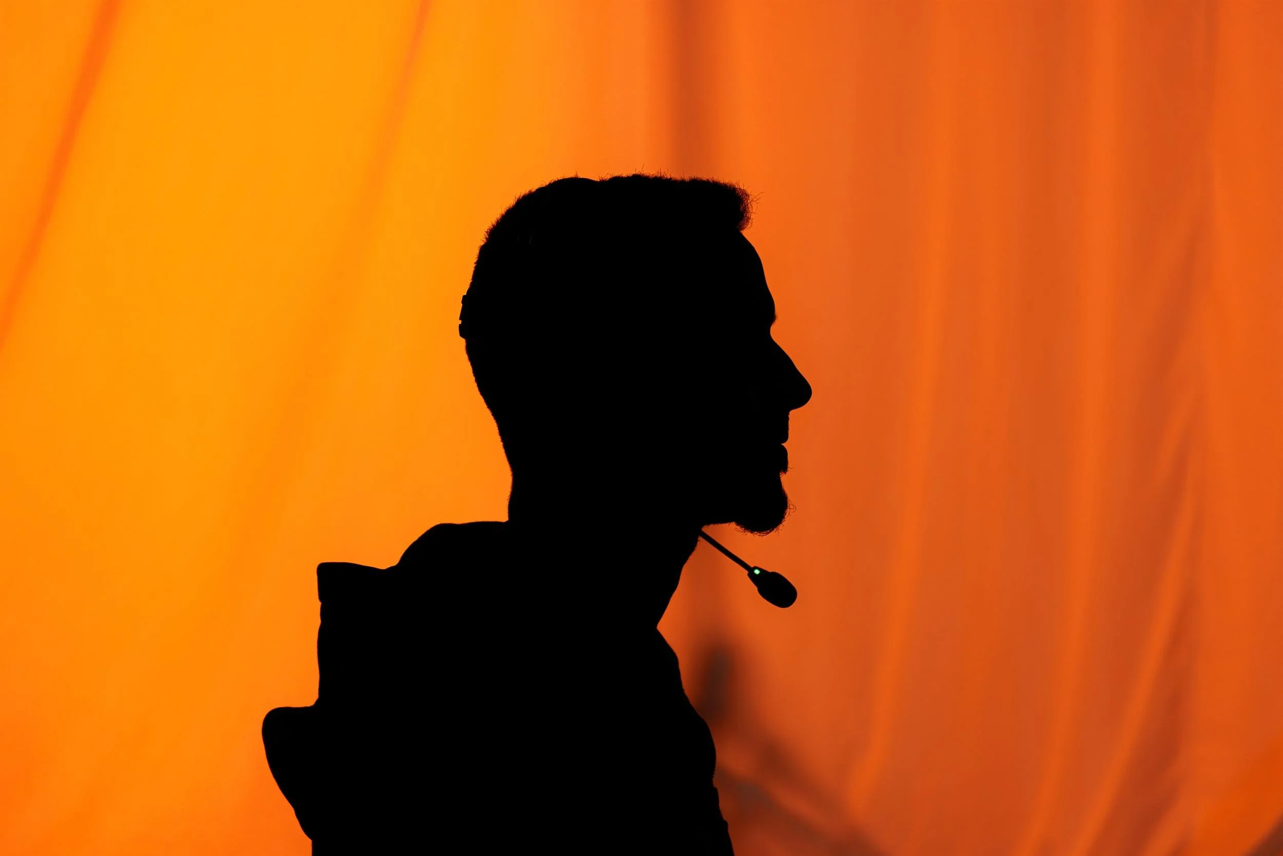 Ahlan Simsim unit still: silhouette of a crew member wearing a headset against an orange backdrop.