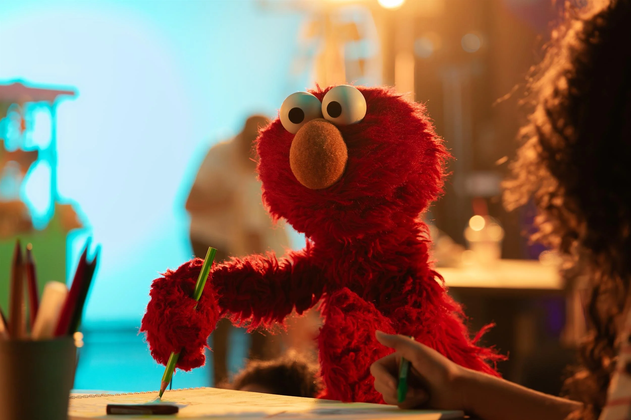 Ahlan Simsim unit still: Elmo writes with a pencil on a studio set.
