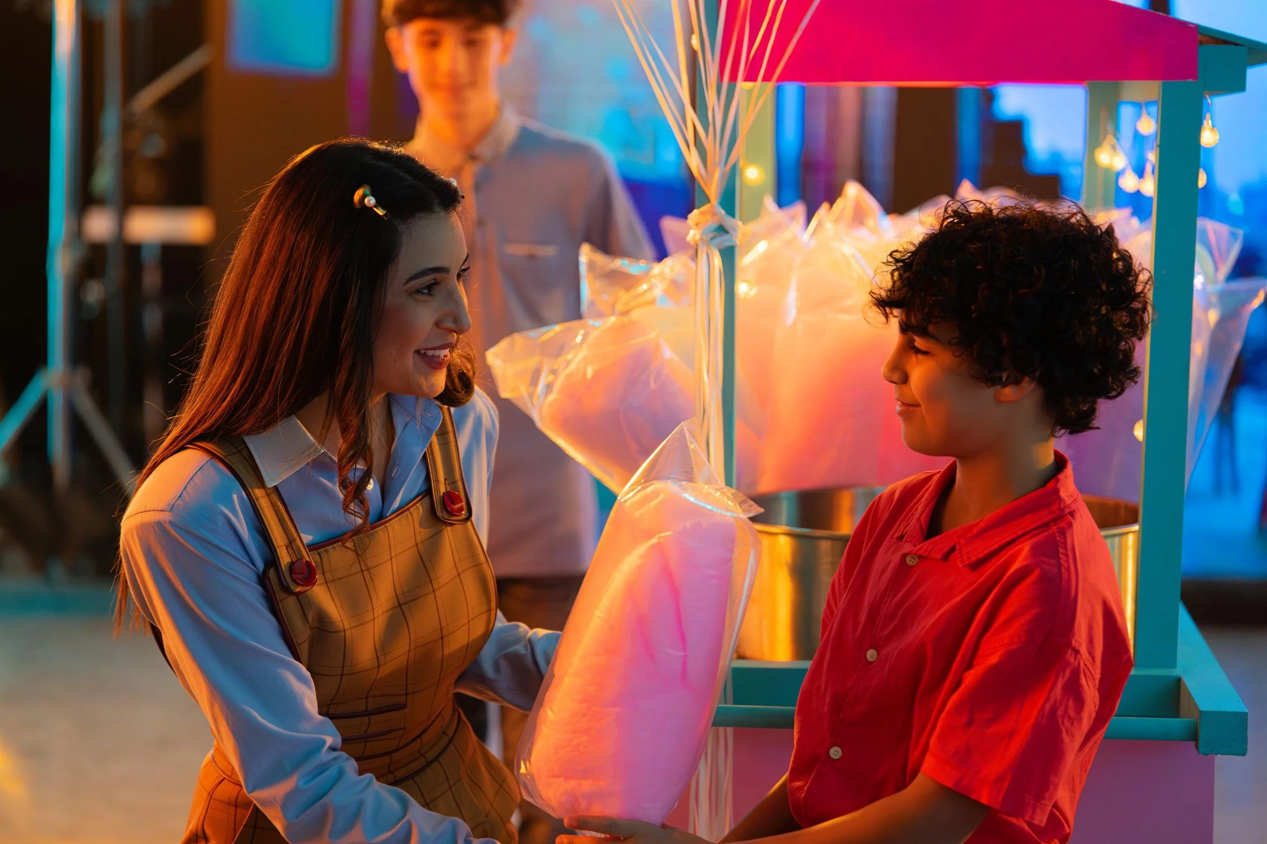 Ahlan Simsim unit still: a woman hands a bag of pink cotton candy to a boy at a market stall.
