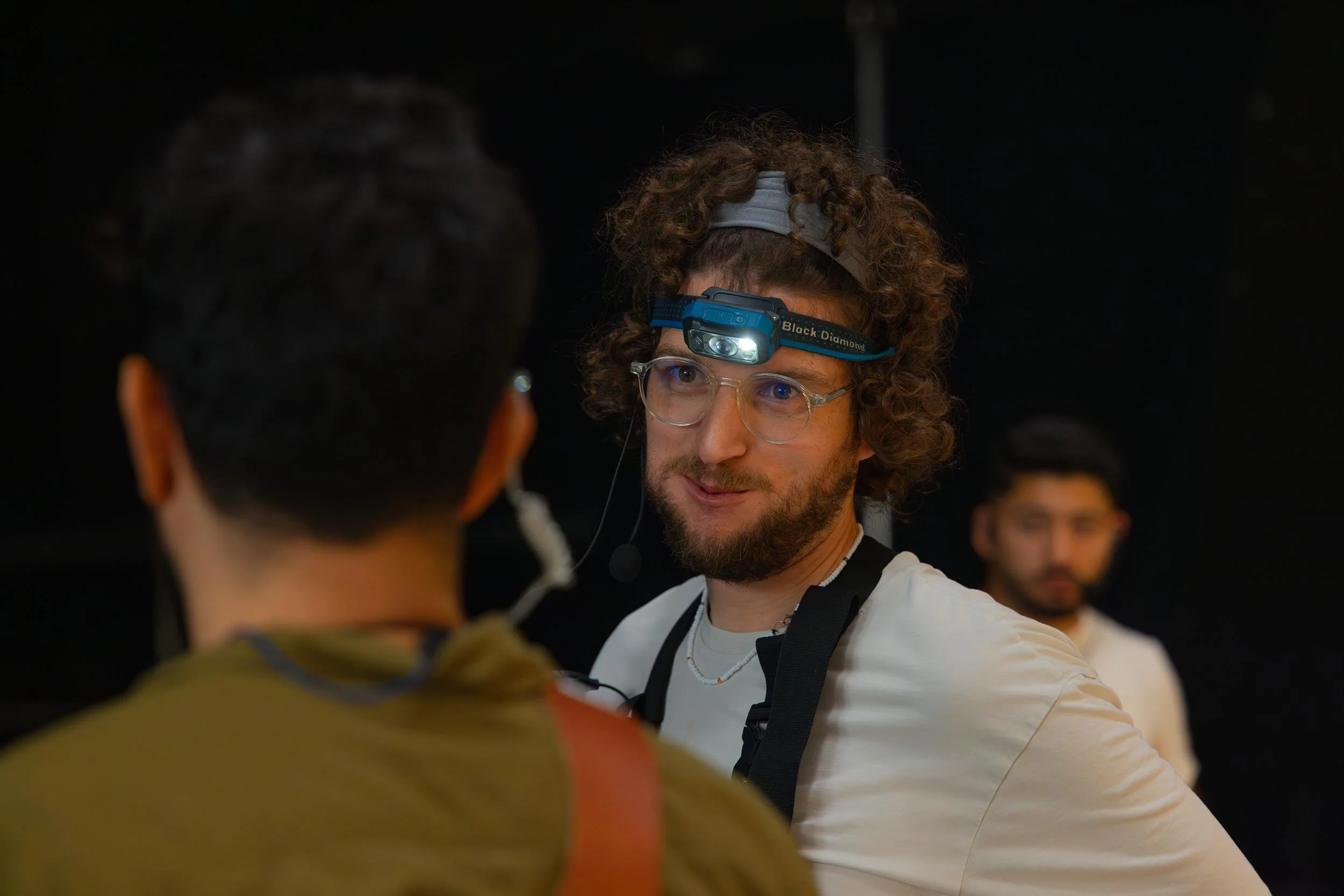 Ahlan Simsim unit still: A crew member with glasses, a headlamp, and a headset works on a dark set.